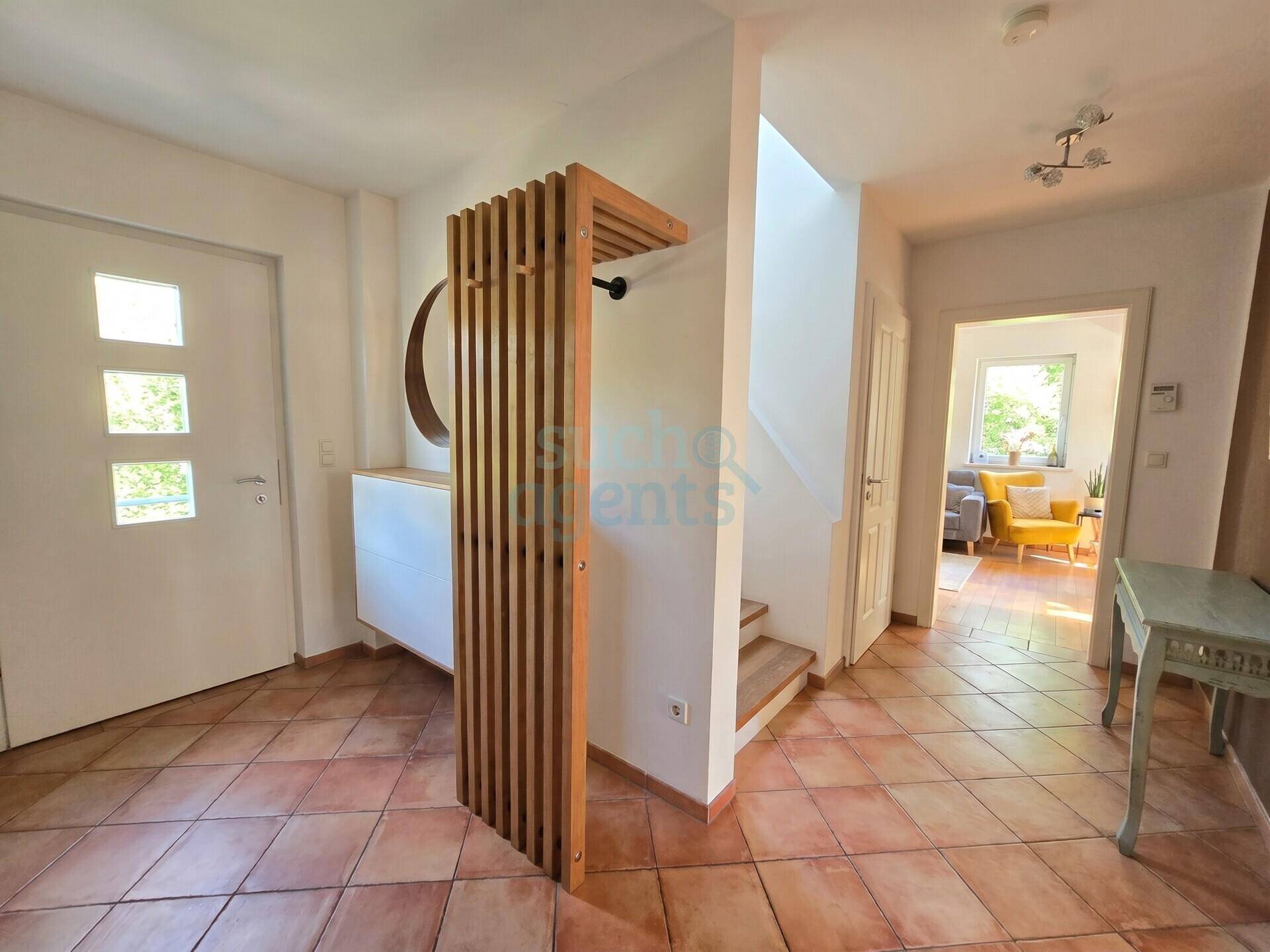Heller Eingangsbereich mit Terrakottafliesen und einer modernen Holzgarderobe, die in den Wohnbereich führt.