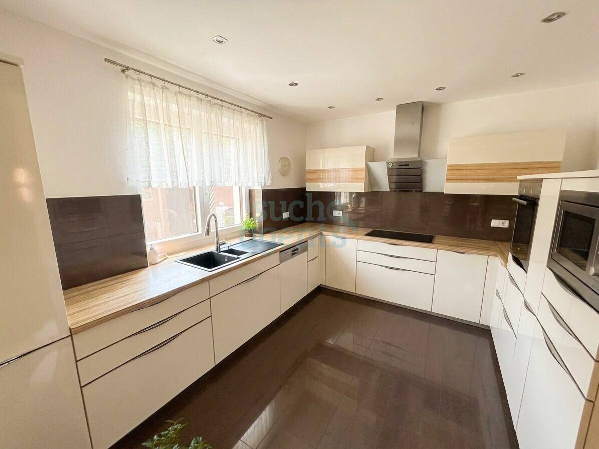 Moderne Einbauküche mit weißen Hochglanzfronten, Holz-Arbeitsplatten und Fenster für Tageslicht.