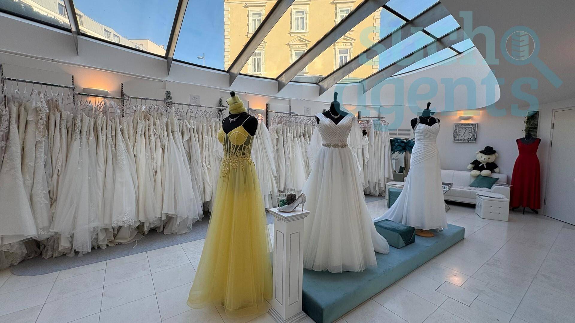 Geräumiger Brautmodenladen mit verschiedenen Hochzeitskleidern auf Schaufensterpuppen und natürlicher Beleuchtung durch das Glasdach.