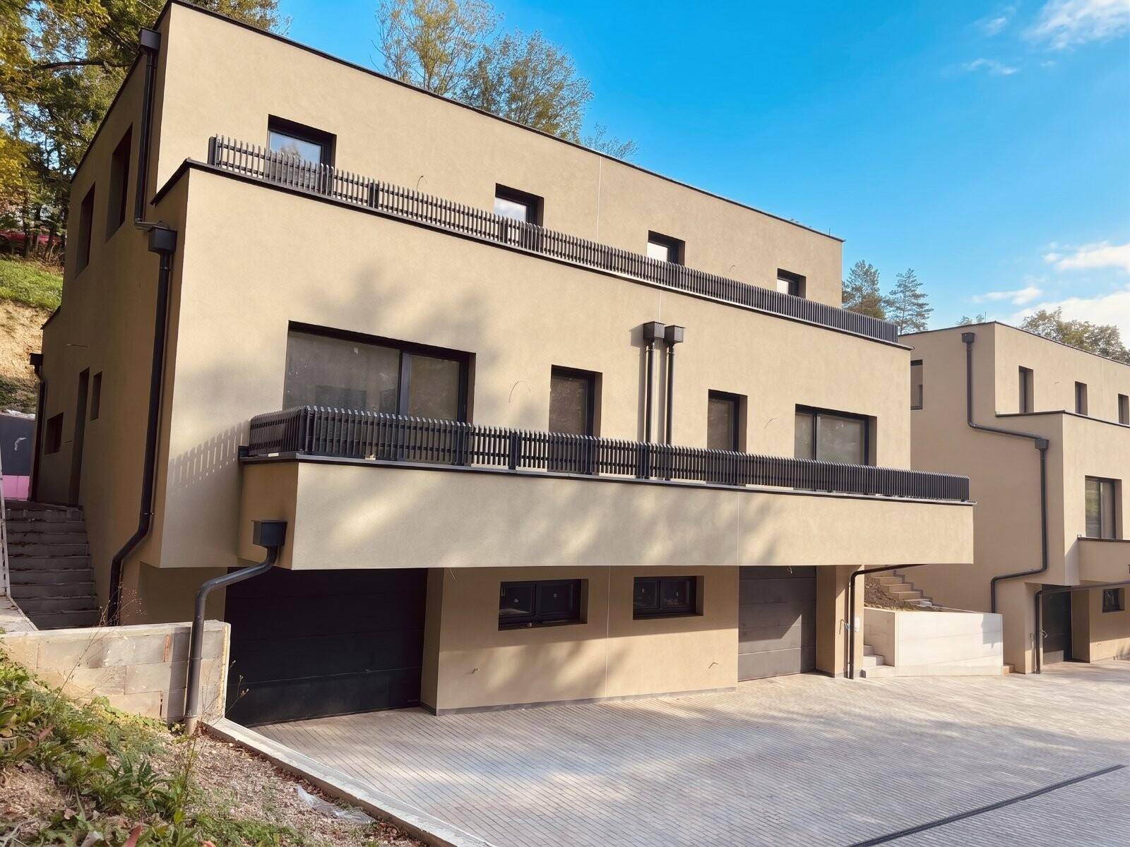 Moderne Wohngebäude mit beiger Fassade, schwarzen Balkongeländern und integrierten Garagen.