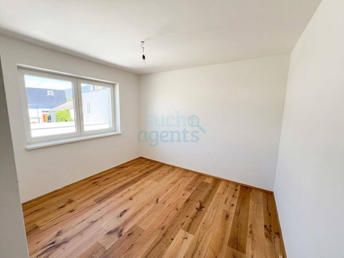 Leeres Schlafzimmer mit Holzboden und einem Fenster, das viel Tageslicht hereinlässt.