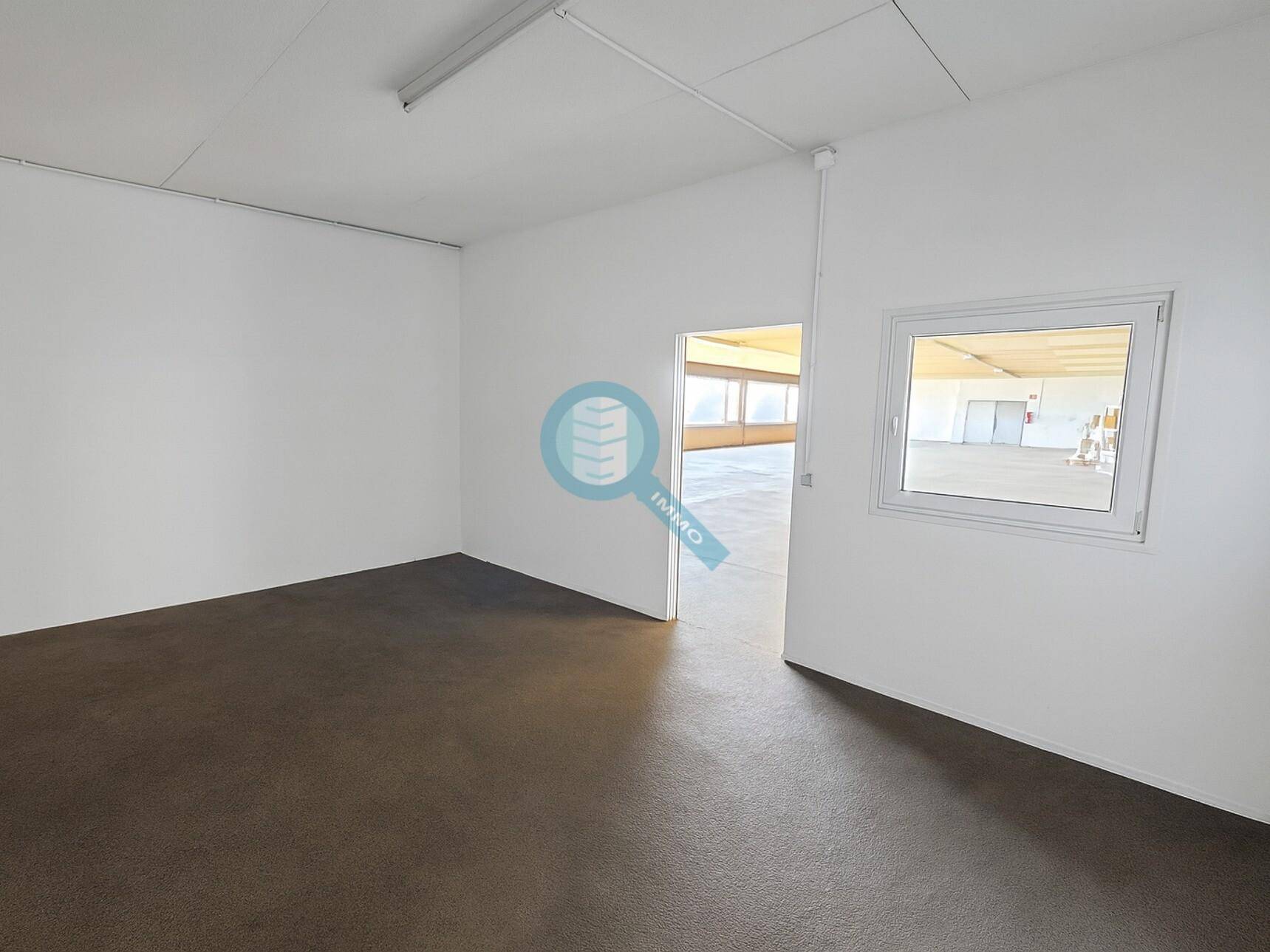 Leerer Raum mit Fenster und Zugang zu einem weiteren großen Gewerbebereich, ideal für flexible Nutzung.