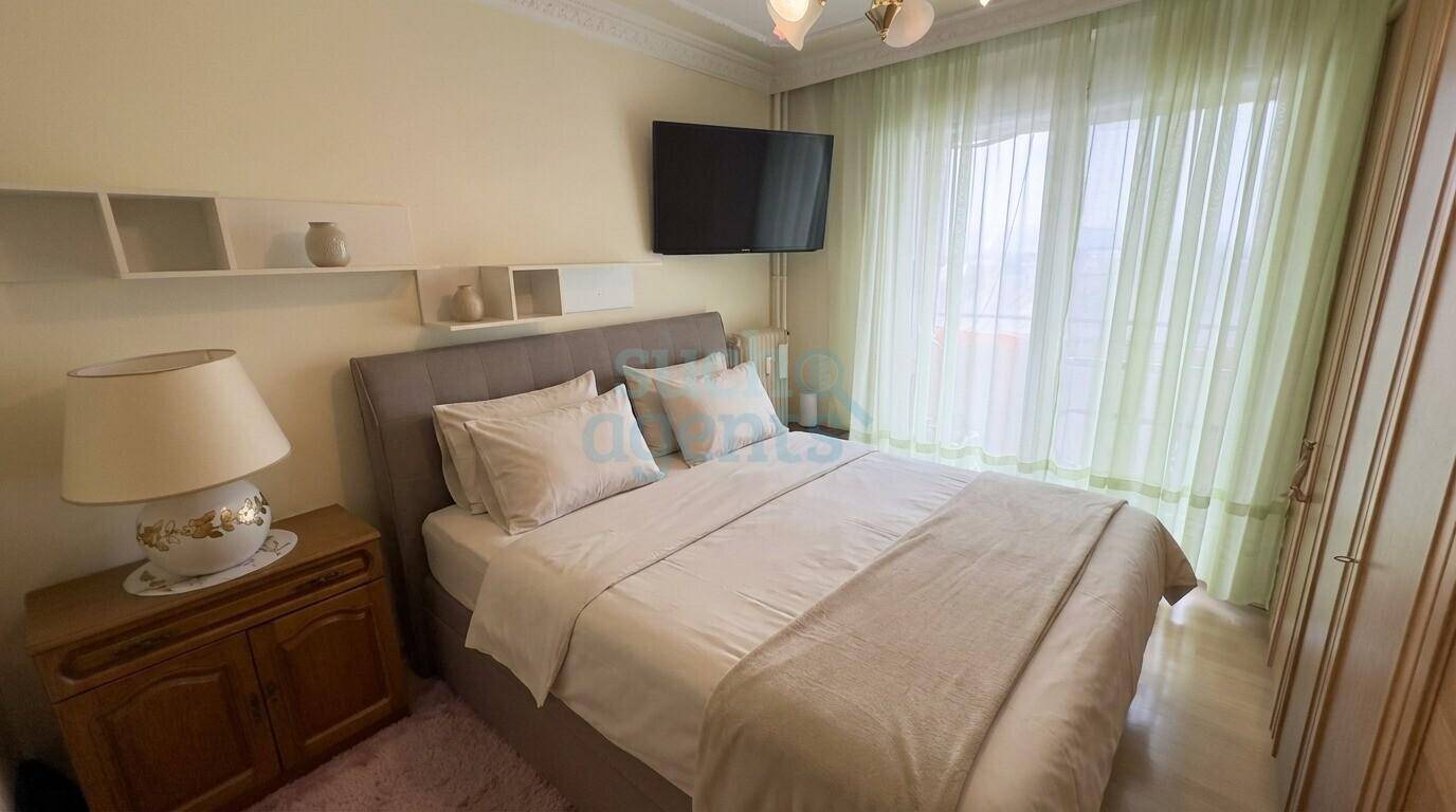 Gemütliches Schlafzimmer mit Doppelbett, hellen Vorhängen und Wandregalen.