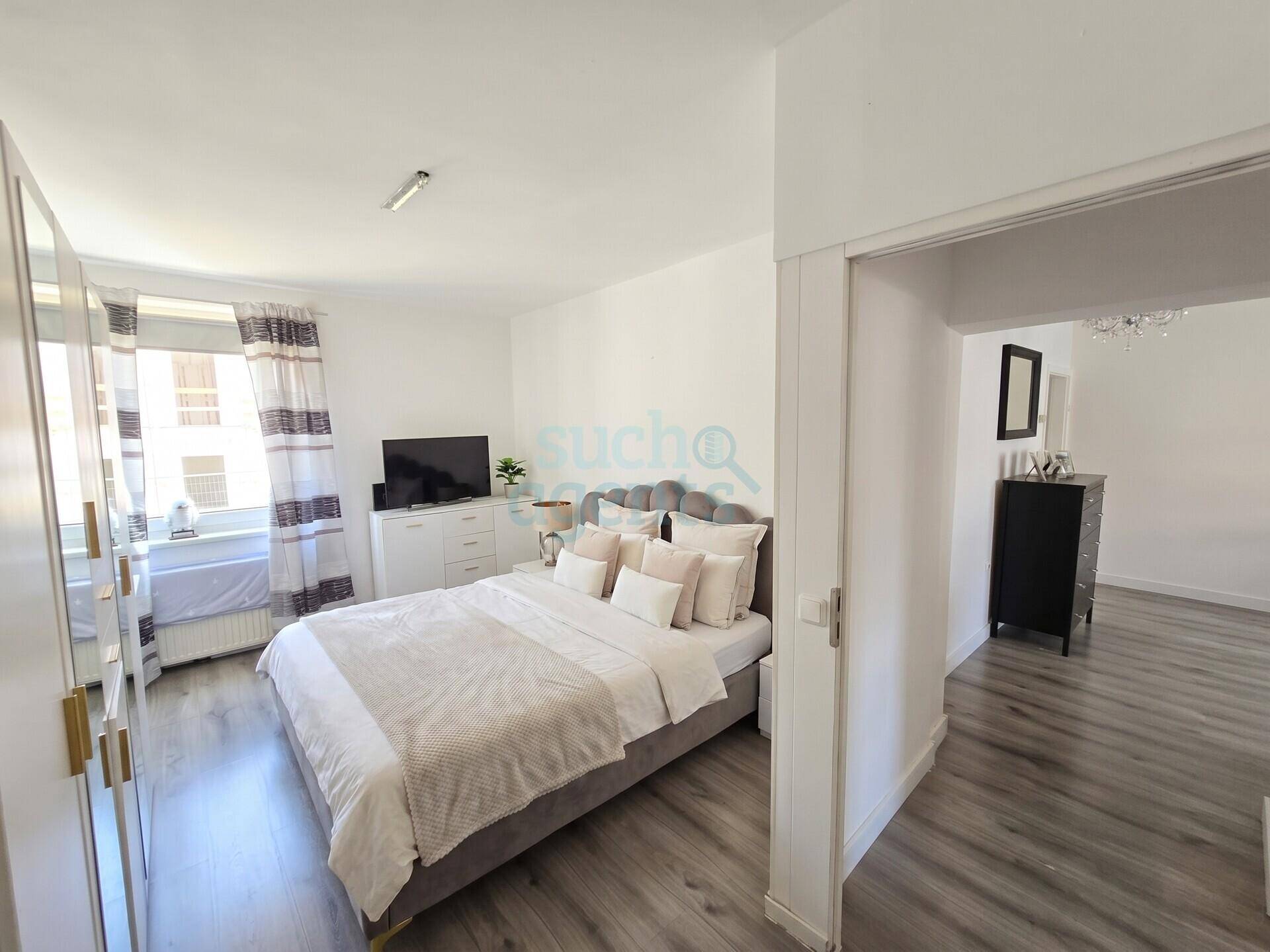 Gemütliches Schlafzimmer mit Laminatboden, großem Bett und Zugang zu einem weiteren Raum.