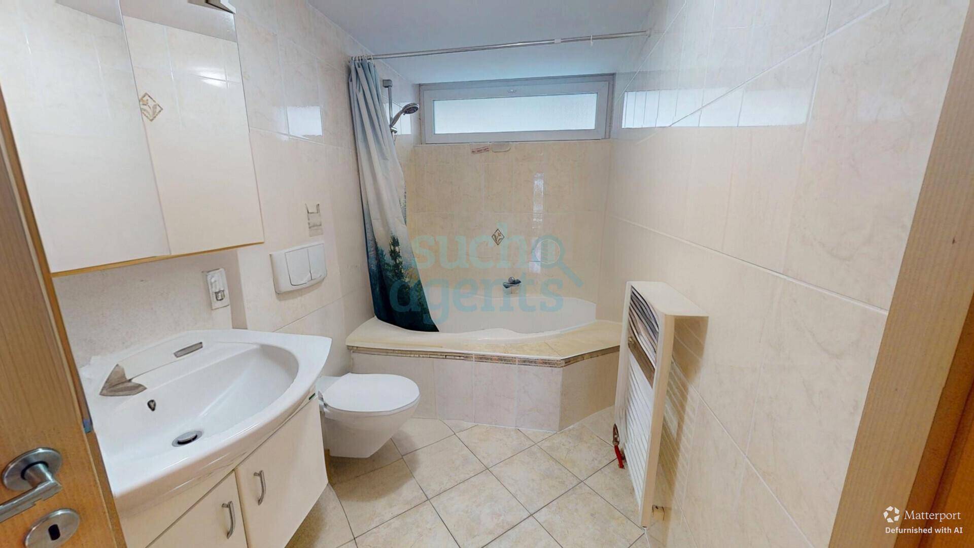 Gefliestes Badezimmer mit Badewanne, Duschvorhang, WC und Waschbecken mit Unterschrank.