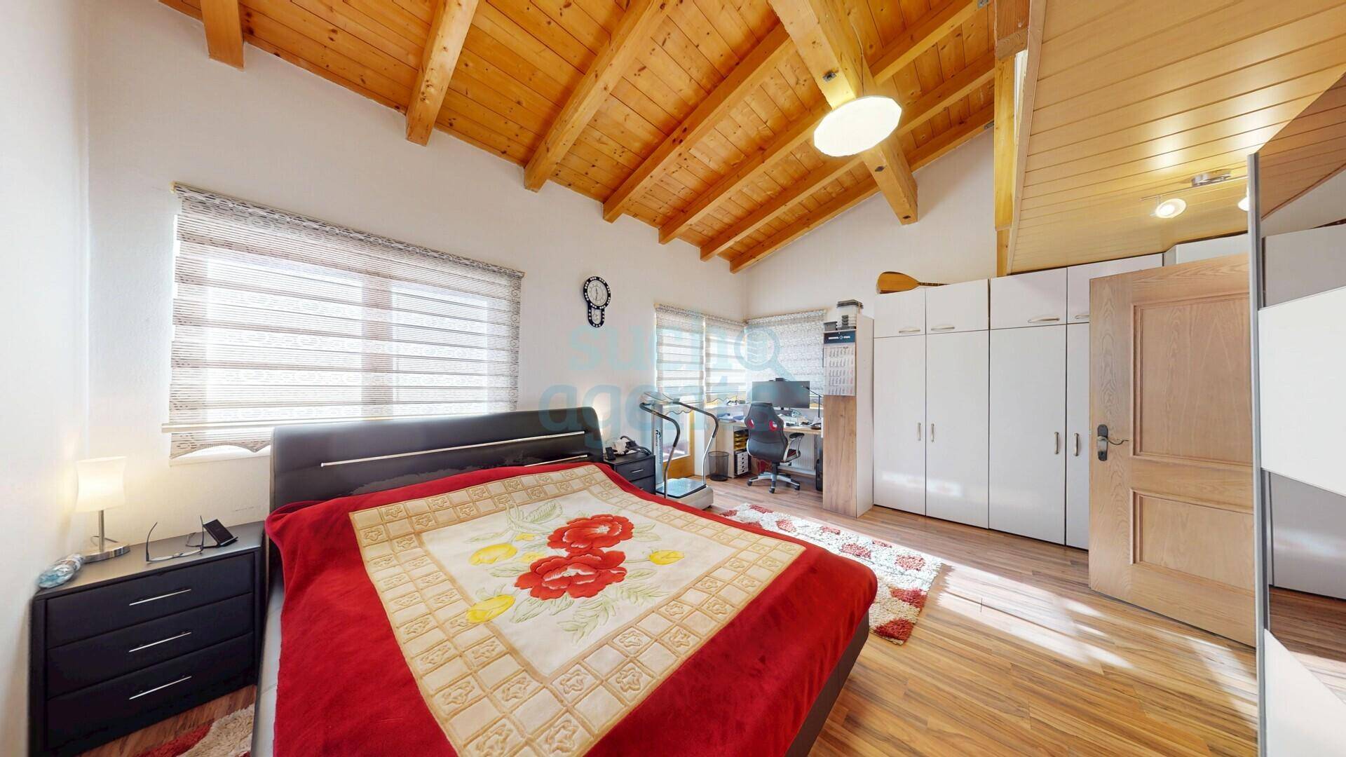 Gemütliches Schlafzimmer mit Holzbalkendecke, großem Bett und integriertem Arbeitsbereich.