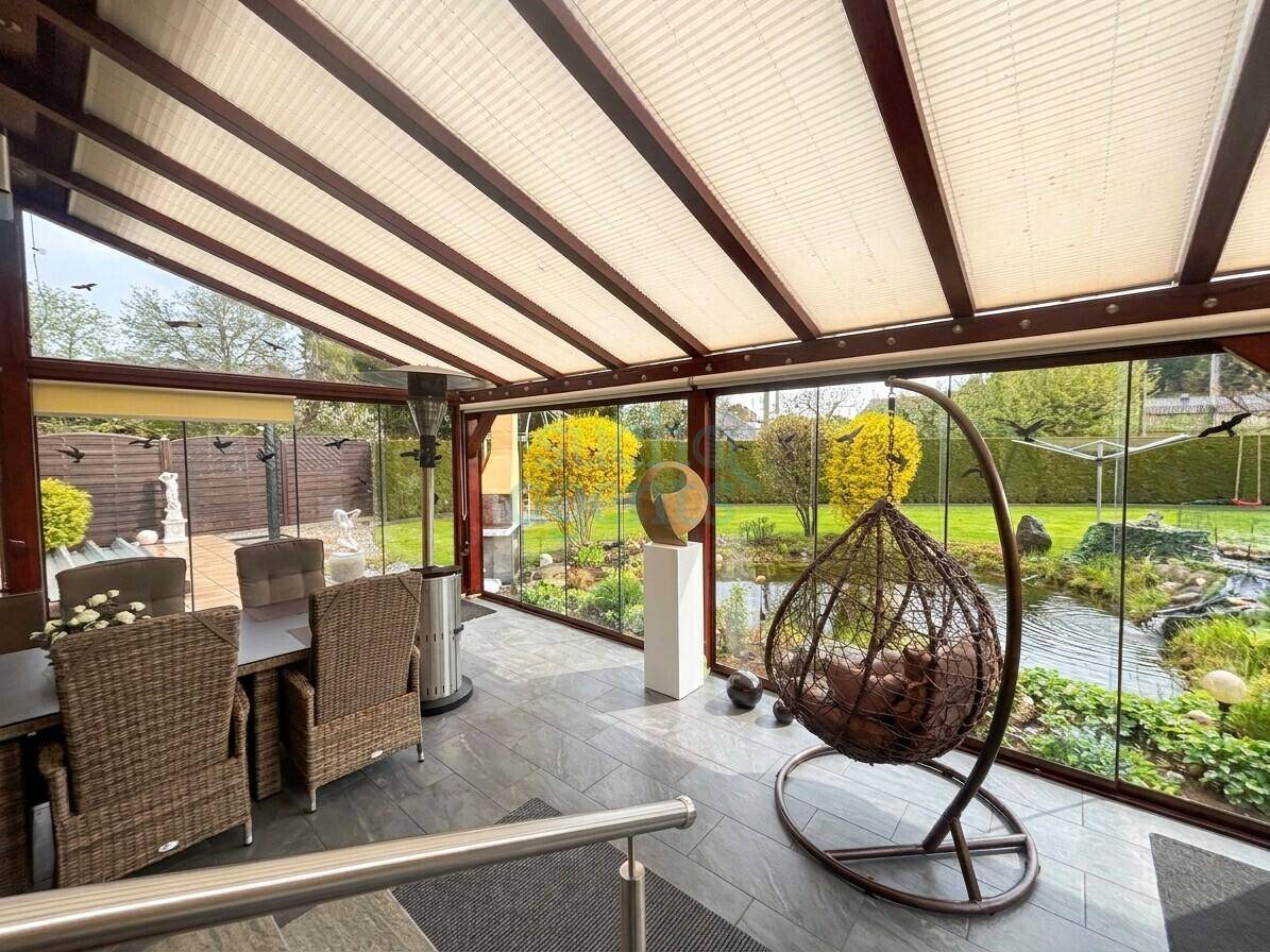 Heller Wintergarten mit Glaswänden, Fliesenboden und gemütlicher Hängesessel-Lounge mit Gartenblick.