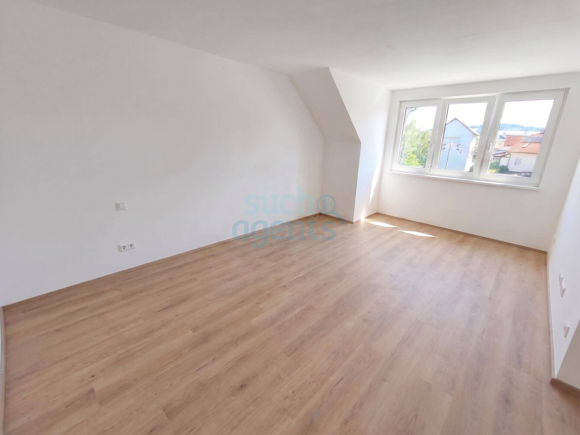 Geräumiges, helles Zimmer mit schrägen Wänden und großen Fenstern, die viel Tageslicht hereinlassen.