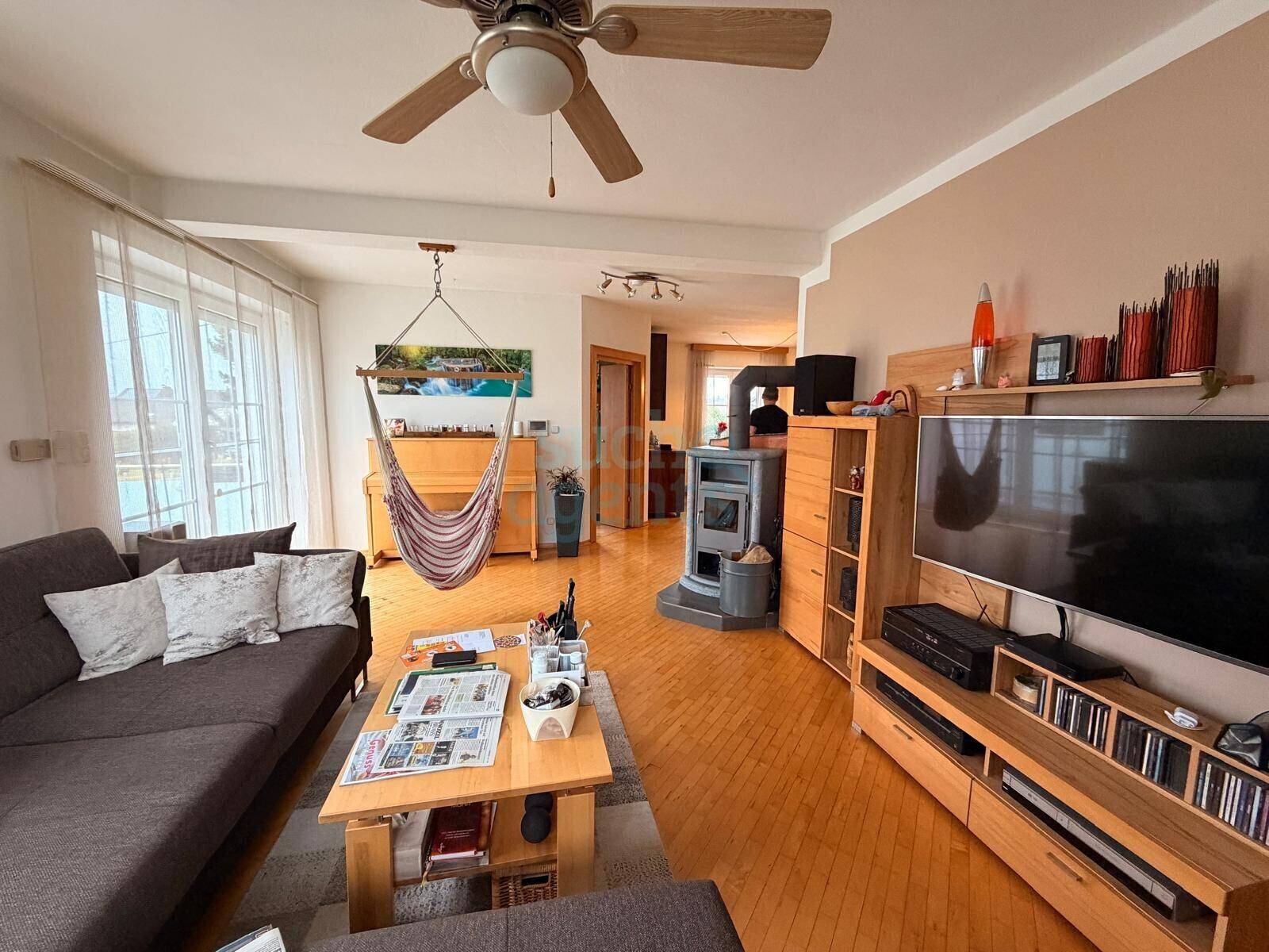 Geräumiges Wohnzimmer mit Holzofen, Parkettboden und Zugang zu einem hellen Bereich.