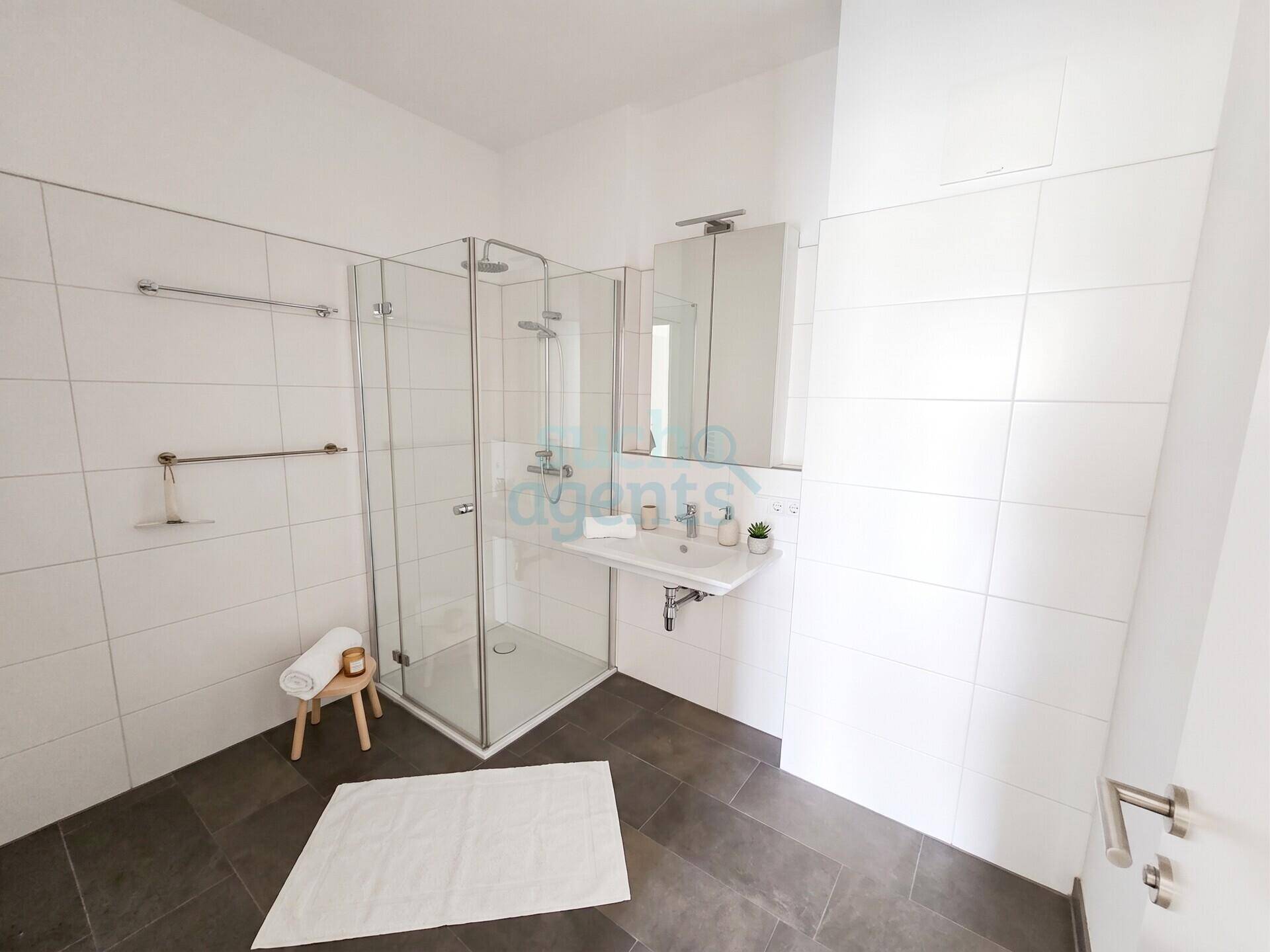 Modernes Badezimmer mit großer begehbarer Dusche, weißen Fliesen und dunklem Boden.