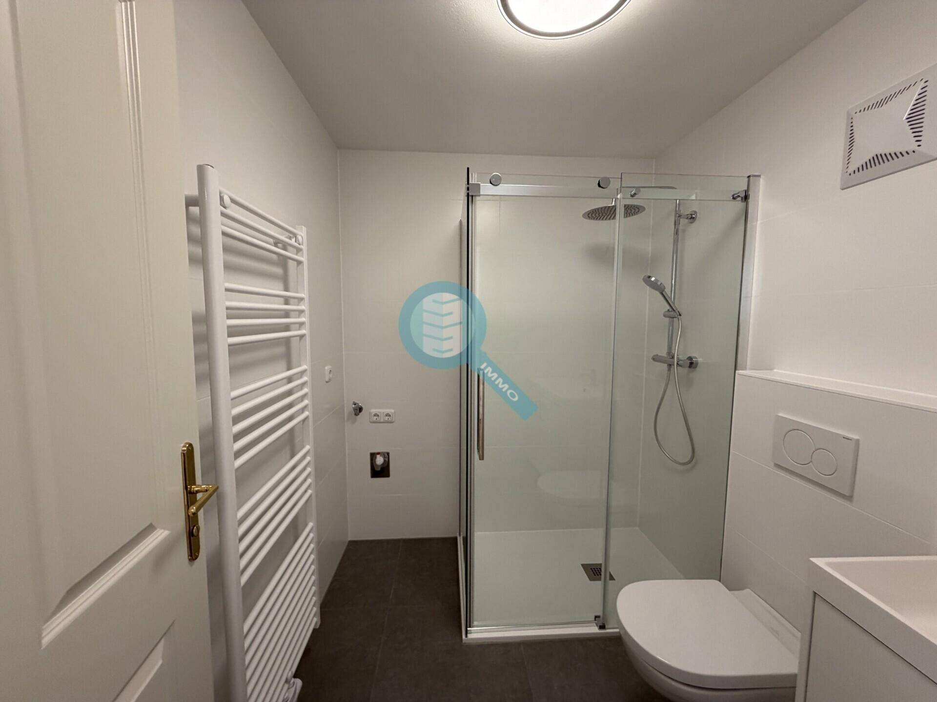 Modernes Badezimmer mit ebenerdiger Dusche, wandhängendem WC und beheiztem Handtuchhalter.
