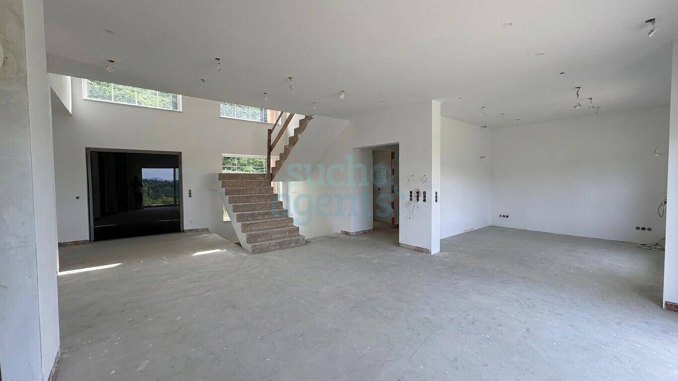 Unfertiger, heller Innenraum mit großer Treppe und viel Tageslicht durch große Fenster.