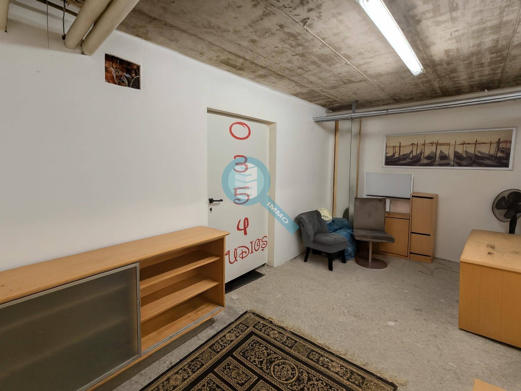 Einfacher Raum mit Beton-Decke, weißen Wänden und einem Teppich, möglicherweise ein Lager- oder Hobbyraum.