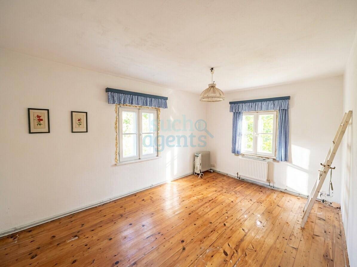 Gemütliches Zimmer mit Holzboden, weißen Wänden und zwei Fenstern mit karierten Vorhängen.