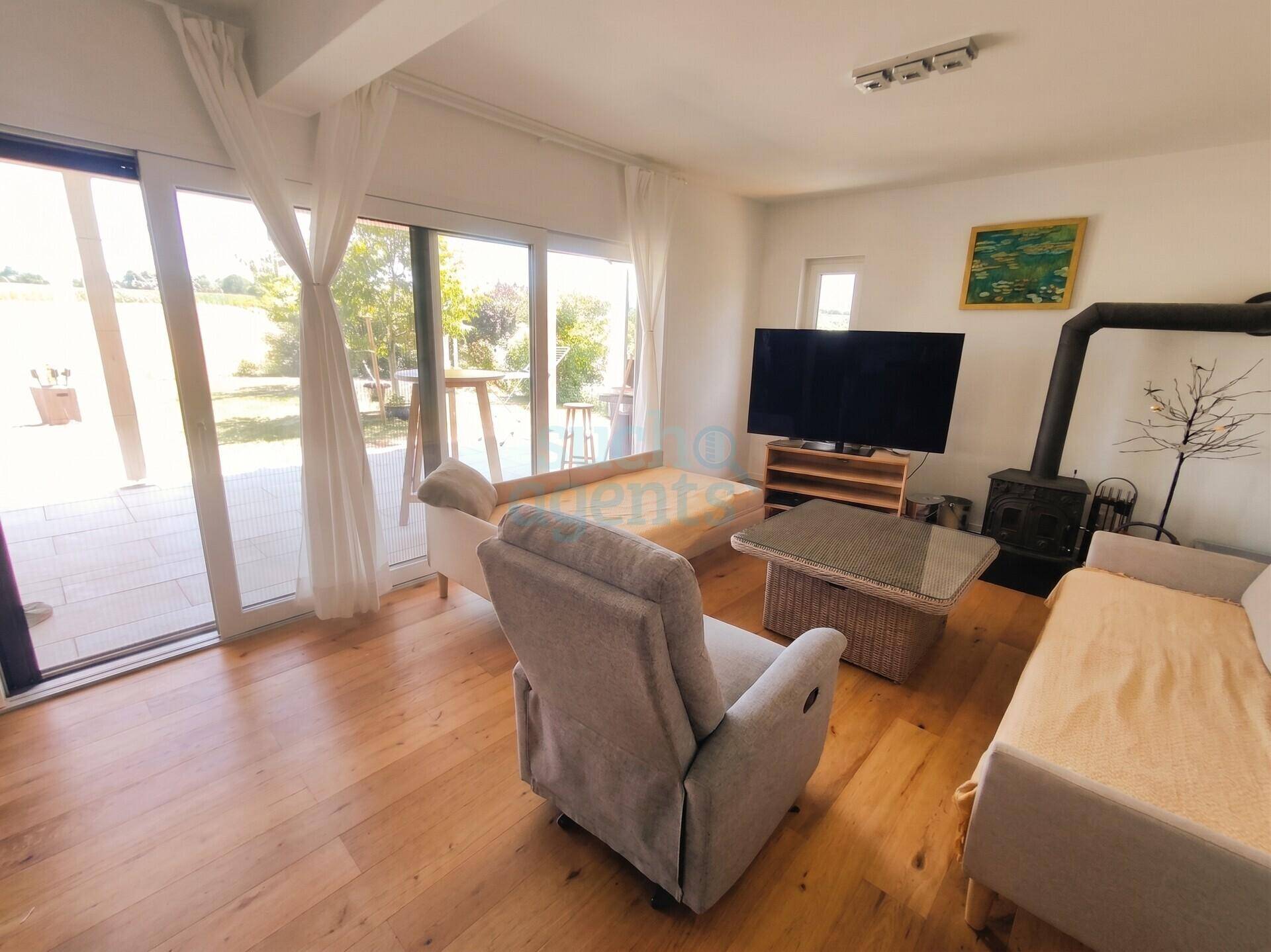 Helles Wohnzimmer mit Holzboden, Kaminofen und großen Glasschiebetüren zum Garten.