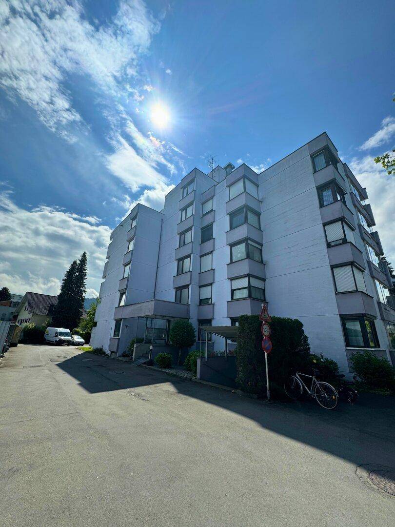 Mehrstöckiges Wohngebäude mit moderner Architektur und vielen Fenstern unter strahlend blauem Himmel.