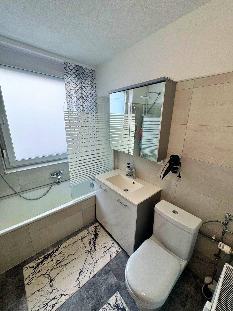 Modernes Badezimmer mit Badewanne, Duschvorhang, Waschbecken und Toilette.