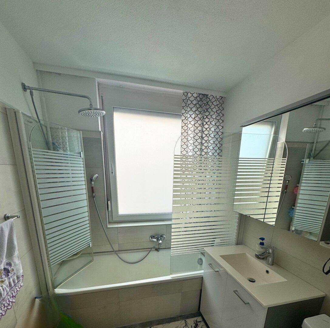 Helles Badezimmer mit Badewanne, integrierter Dusche und einem Fenster für Tageslicht.