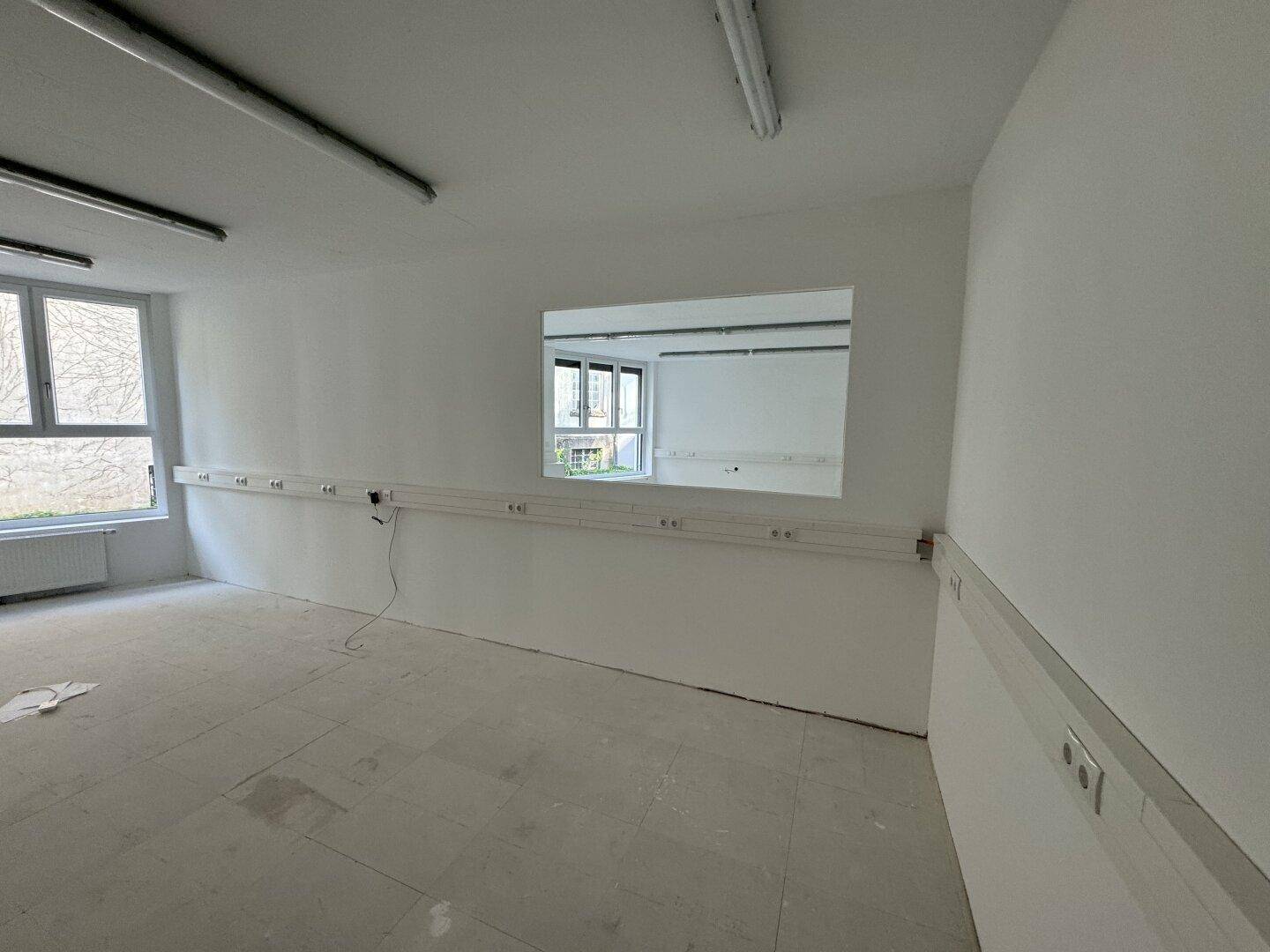 Heller Büroraum mit einem breiten Wandspiegel und Fenstern, die einen Blick auf den Innenhof bieten.