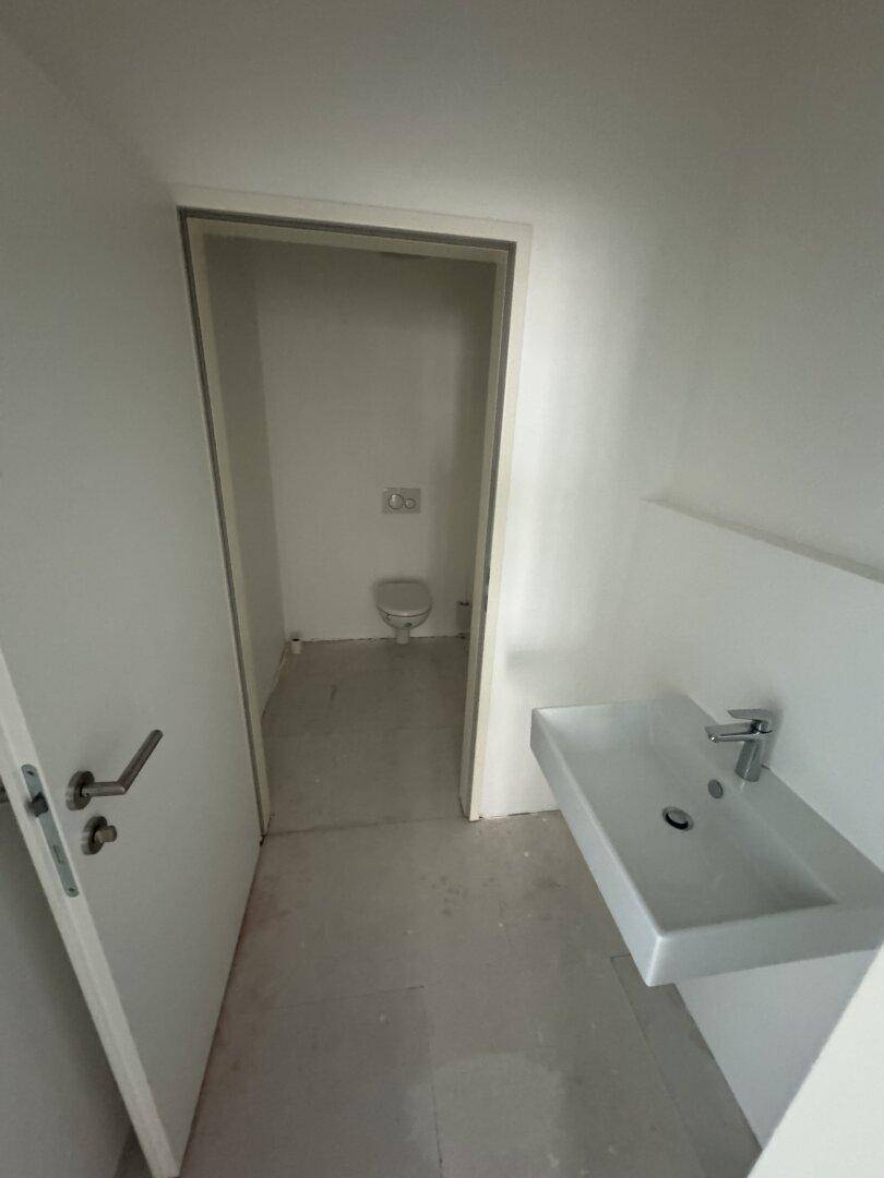 Kleiner, heller Toilettenraum mit modernem Waschbecken und einer separaten WC-Kabine im Hintergrund.