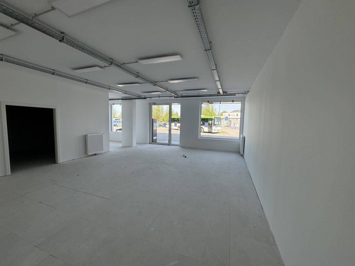 Geräumiger Büroraum mit viel Tageslicht durch große Fenster und einer funktionalen Deckenbeleuchtung.