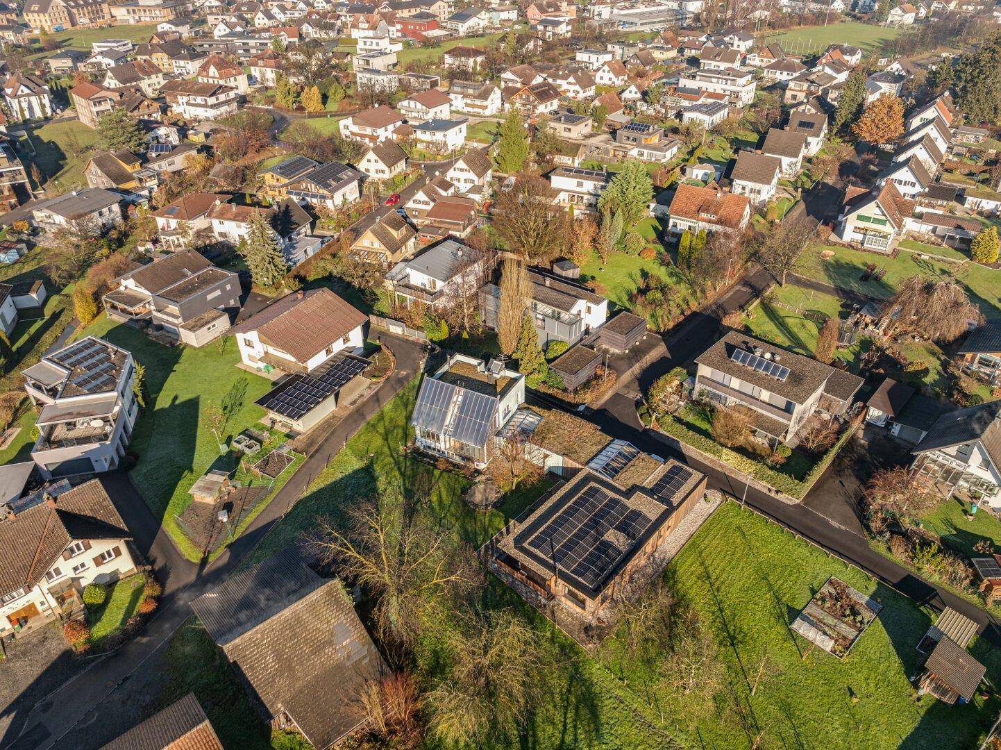 Luftaufnahme einer Wohnsiedlung mit vielen Häusern und grünen Gärten unter blauem Himmel.