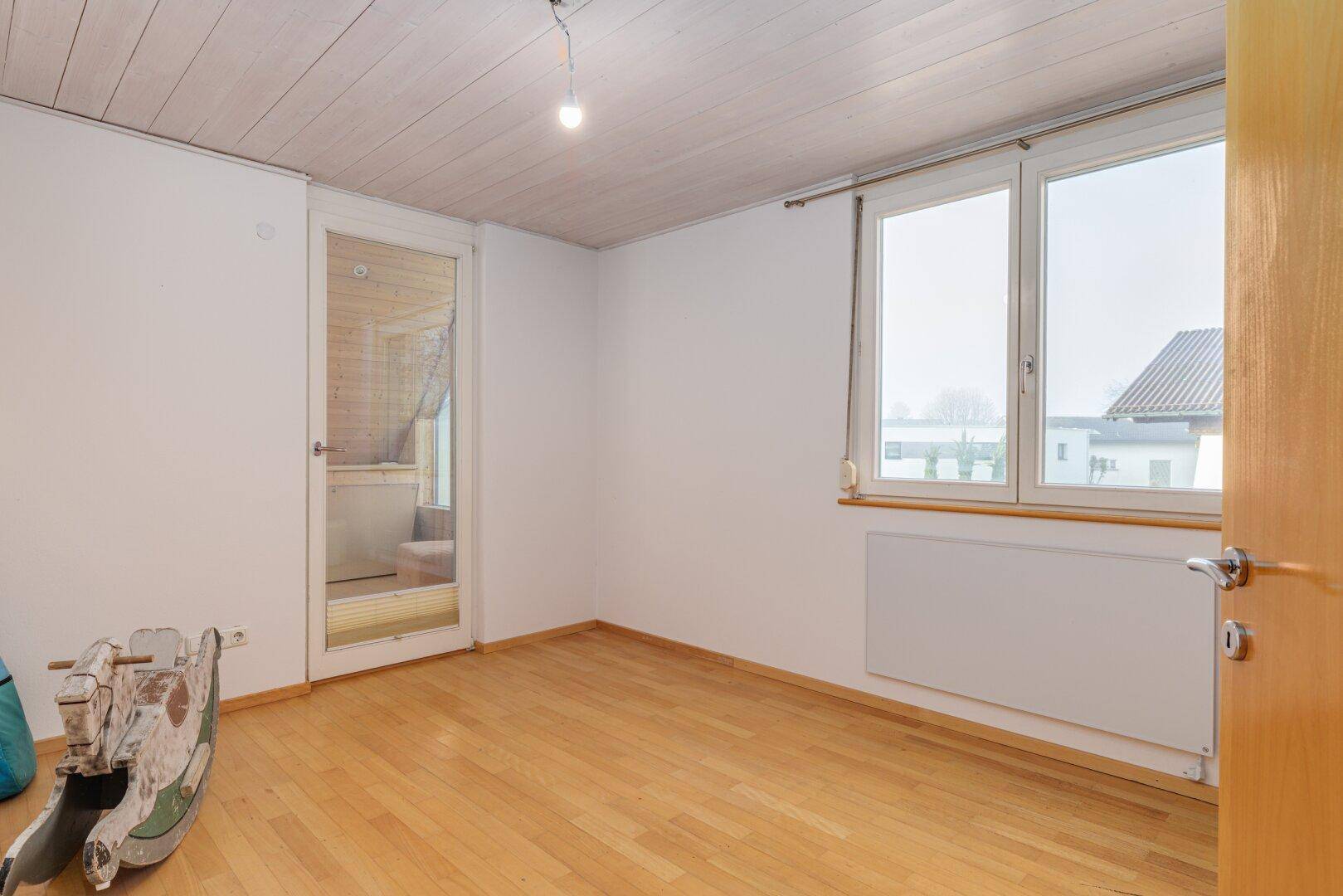 Helles Schlafzimmer mit Holzboden, weißen Wänden und Fenster mit Ausblick.