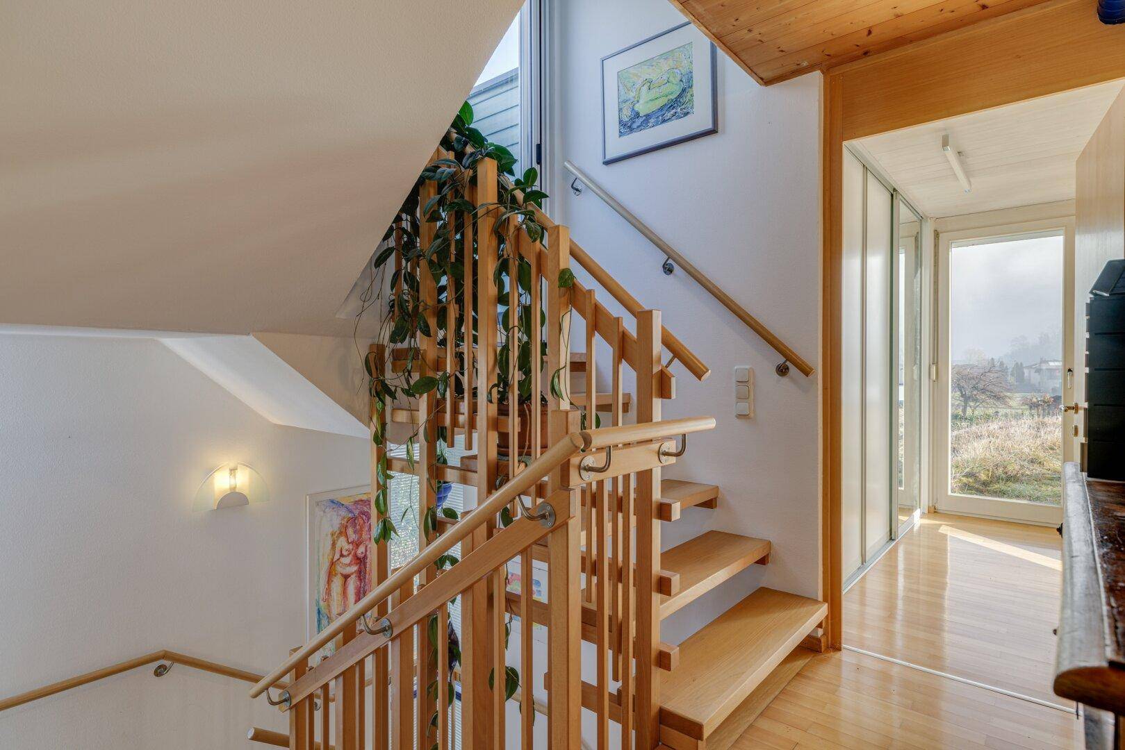 Helles Treppenhaus mit Holzstufen, Pflanzen und Zugang zu einem sonnigen Bereich.