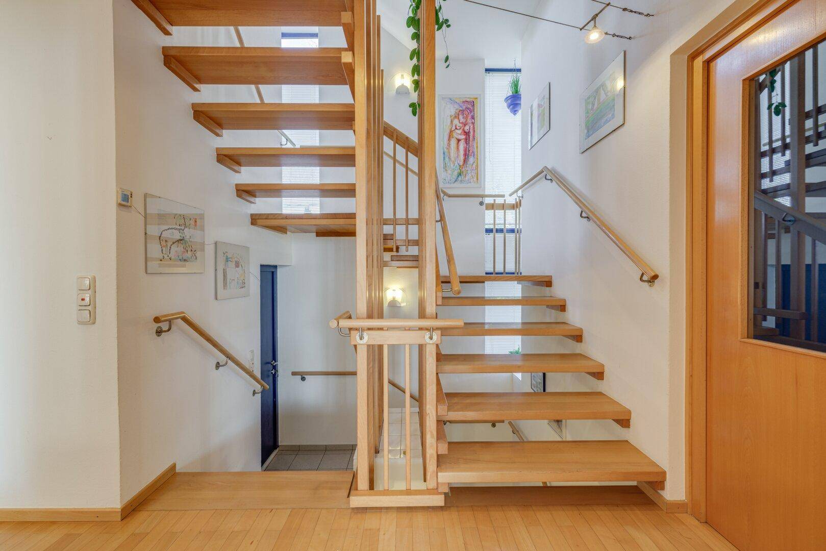 Geräumiges Treppenhaus aus Holz mit natürlichem Lichteinfall und Kunstwerken an den Wänden.