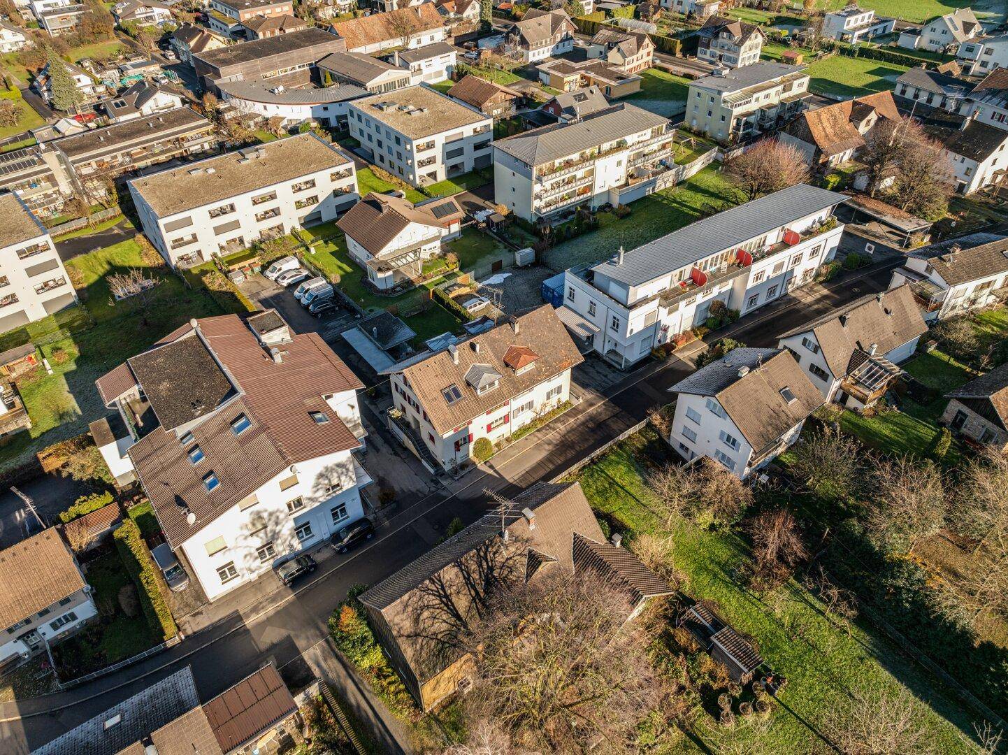 Luftaufnahme einer Wohnsiedlung mit verschiedenen Häusern und Grünflächen unter klarem Himmel.