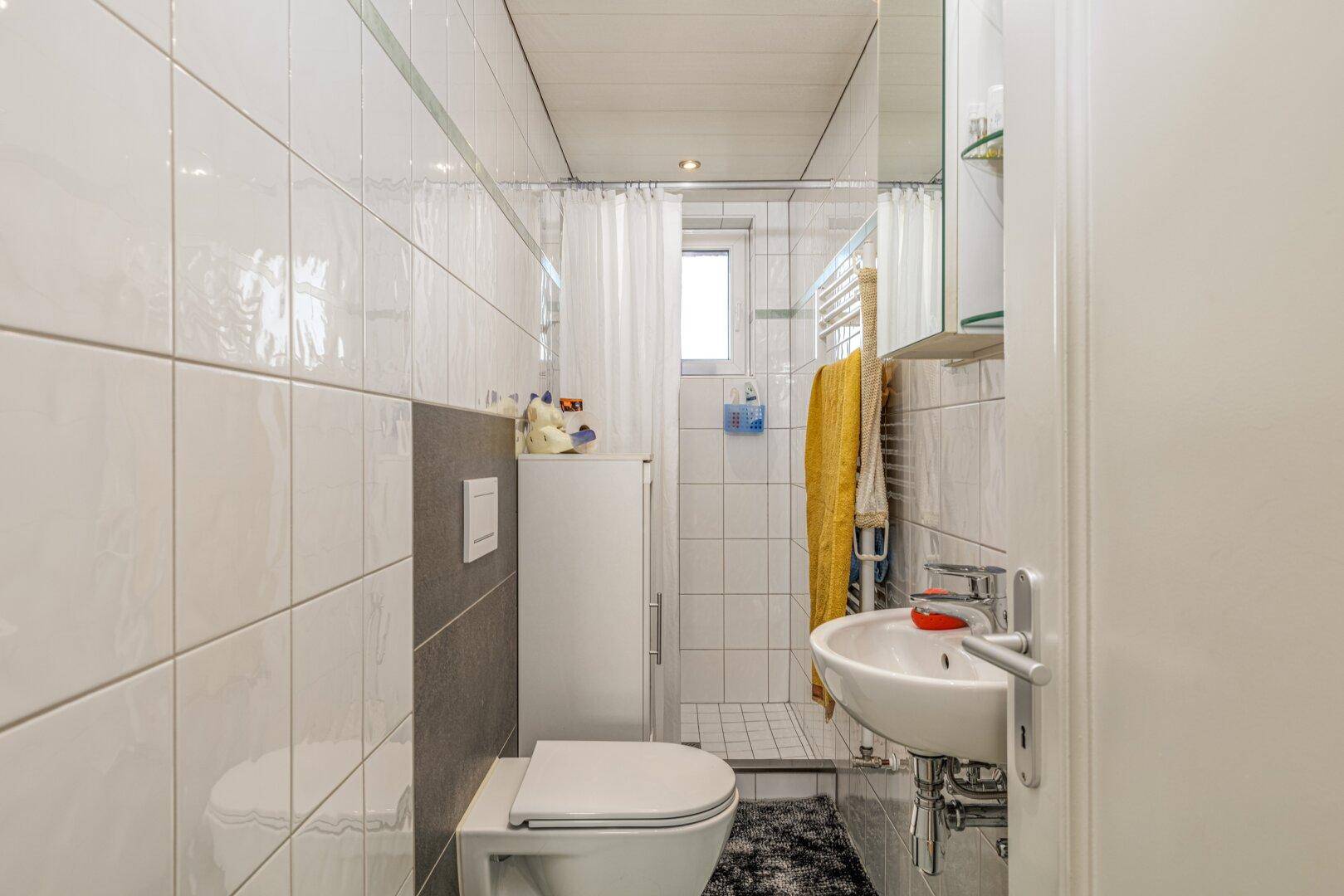 Modernes Badezimmer mit Dusche, WC, Waschbecken und weißen Fliesen.