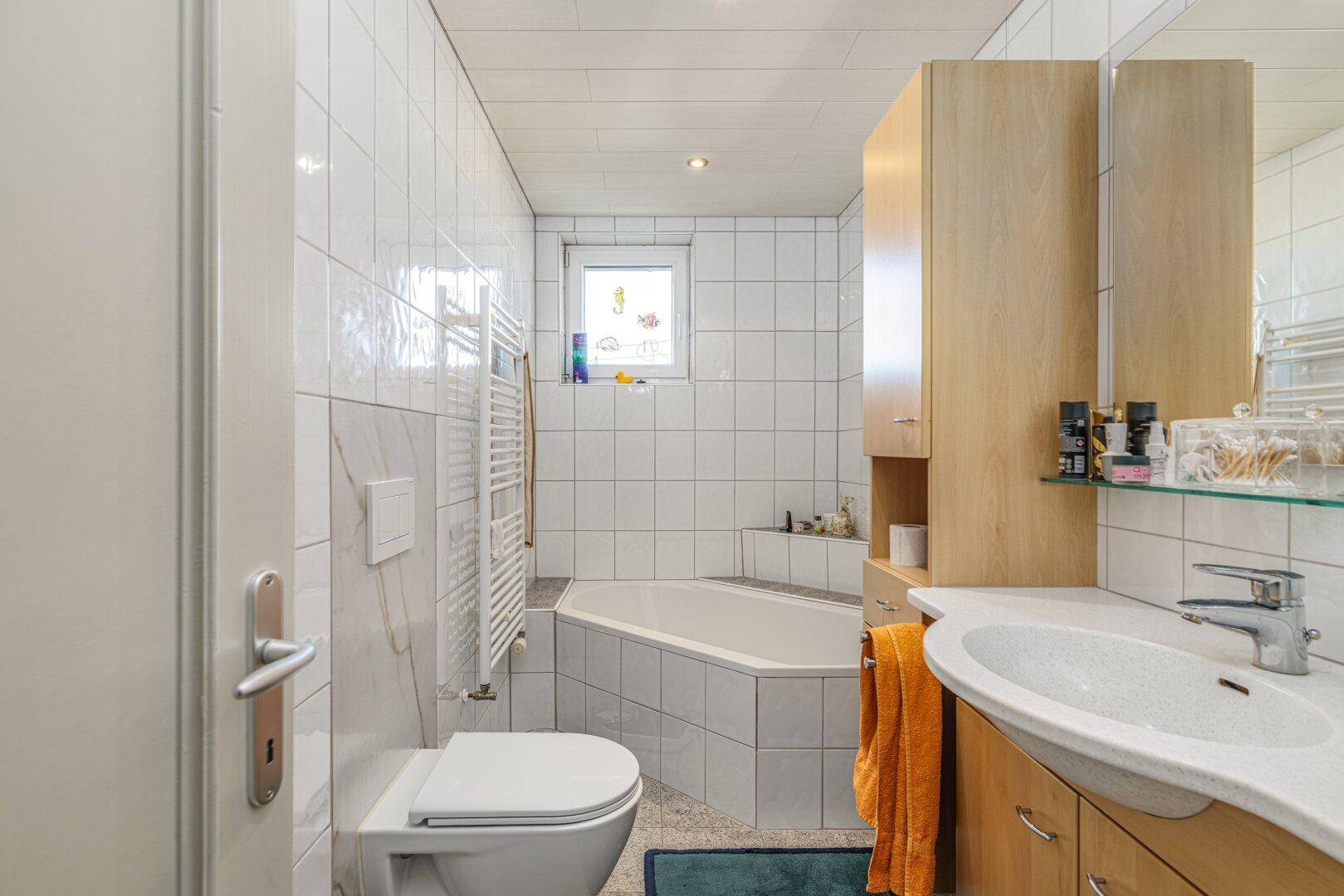 Helles Badezimmer mit Eckbadewanne, WC, Waschbecken und Holzschränken.