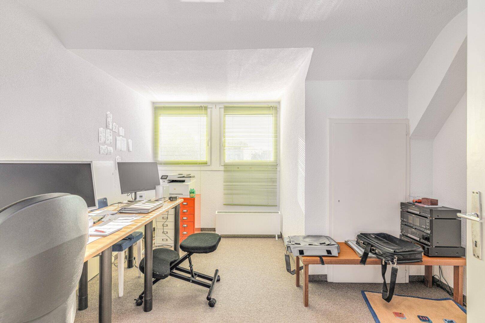 Helles Arbeitszimmer mit zwei Computermonitoren und Teppichboden.