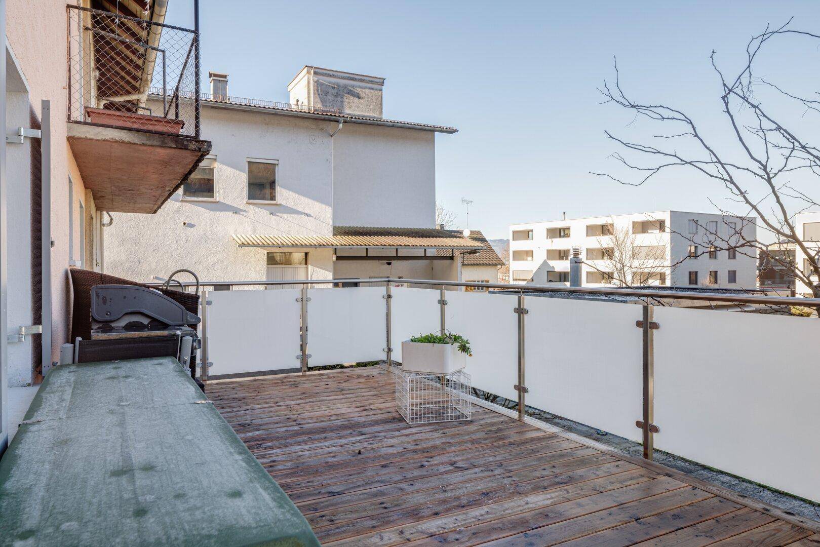 Geräumiger Balkon mit Holzfußboden, Grill und Blick auf die umliegenden Gebäude.