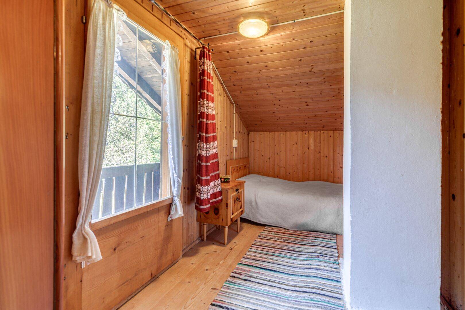 Gemütliches Schlafzimmer mit Holzvertäfelung, Einzelbett und Fenster mit Blick ins Grüne.