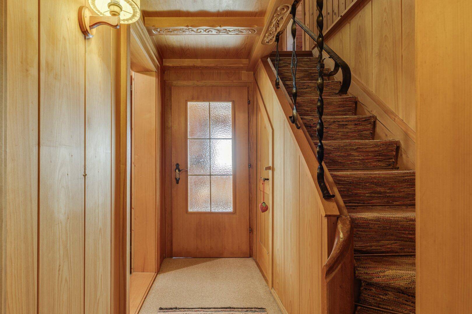 Eingangsbereich mit Holzvertäfelung, Teppichboden auf der Treppe und rustikalem Geländer.