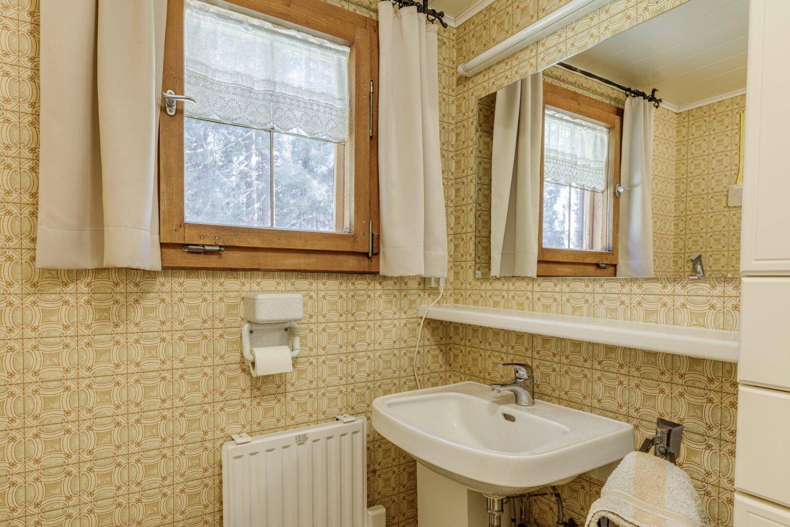 Badezimmer mit beigefarbenen Fliesen, Fenster und einem einzelnen Waschbecken.