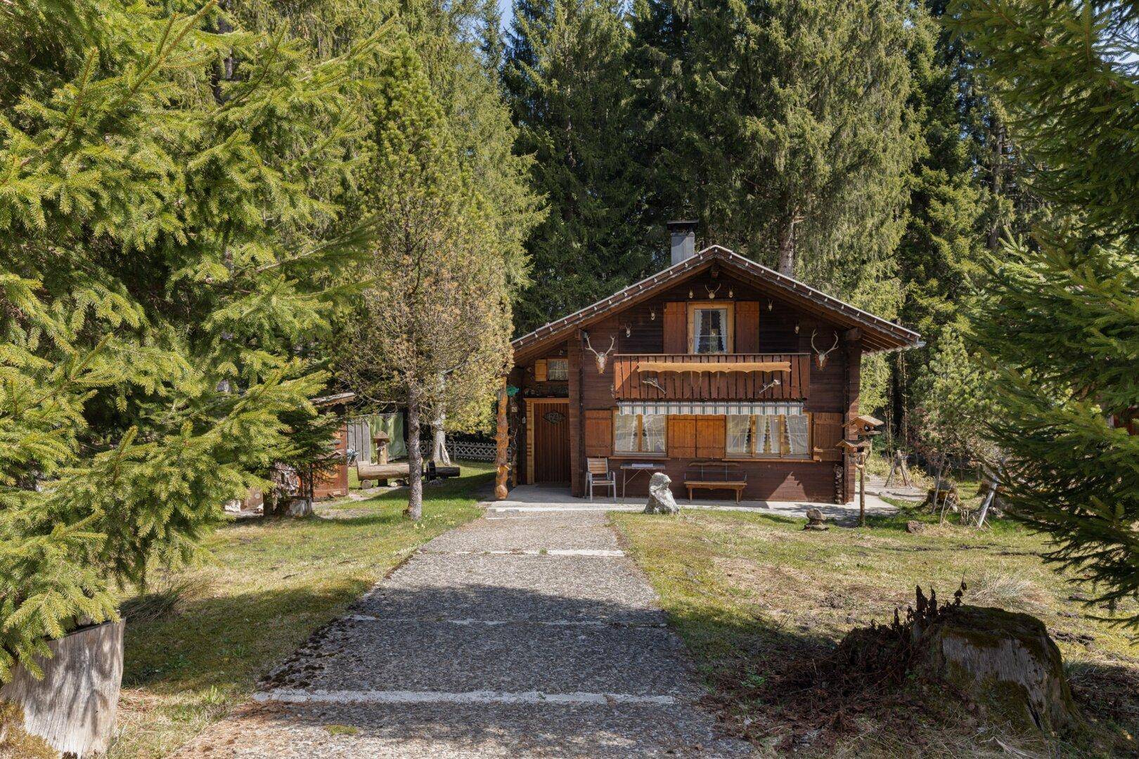 Charmantes Holzhaus mit traditioneller Fassade, umgeben von einem gepflegten Garten und hohen Bäumen.