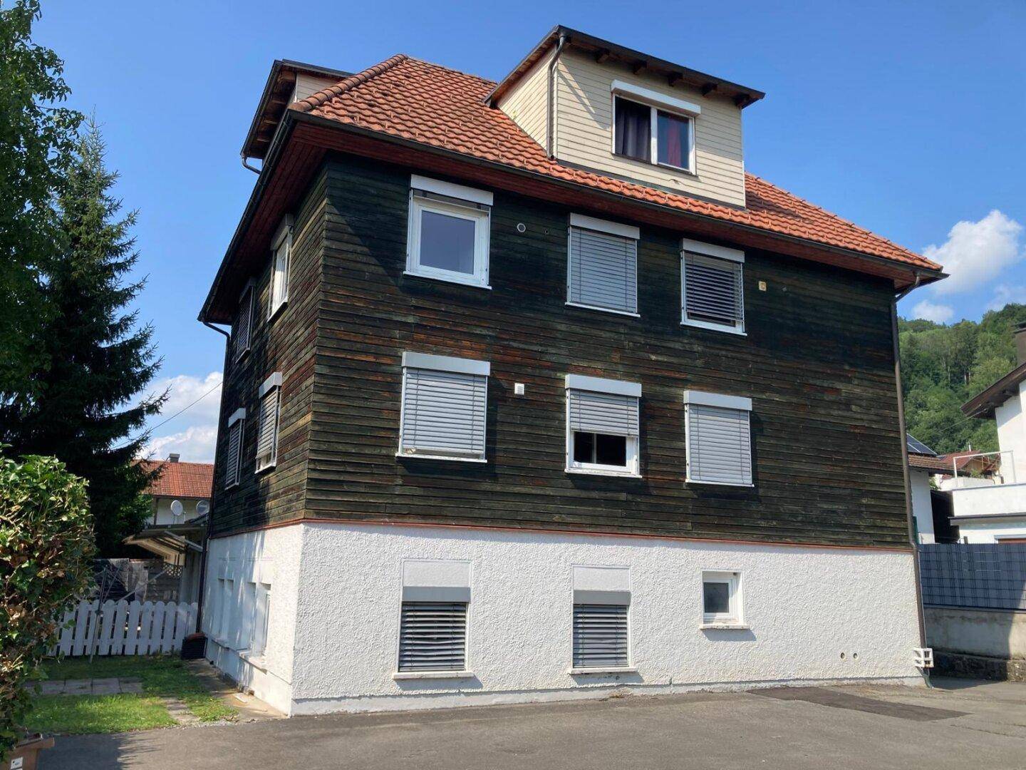 Seitenansicht des Mehrfamilienhauses mit Holzfassade und Rollläden an den Fenstern.
