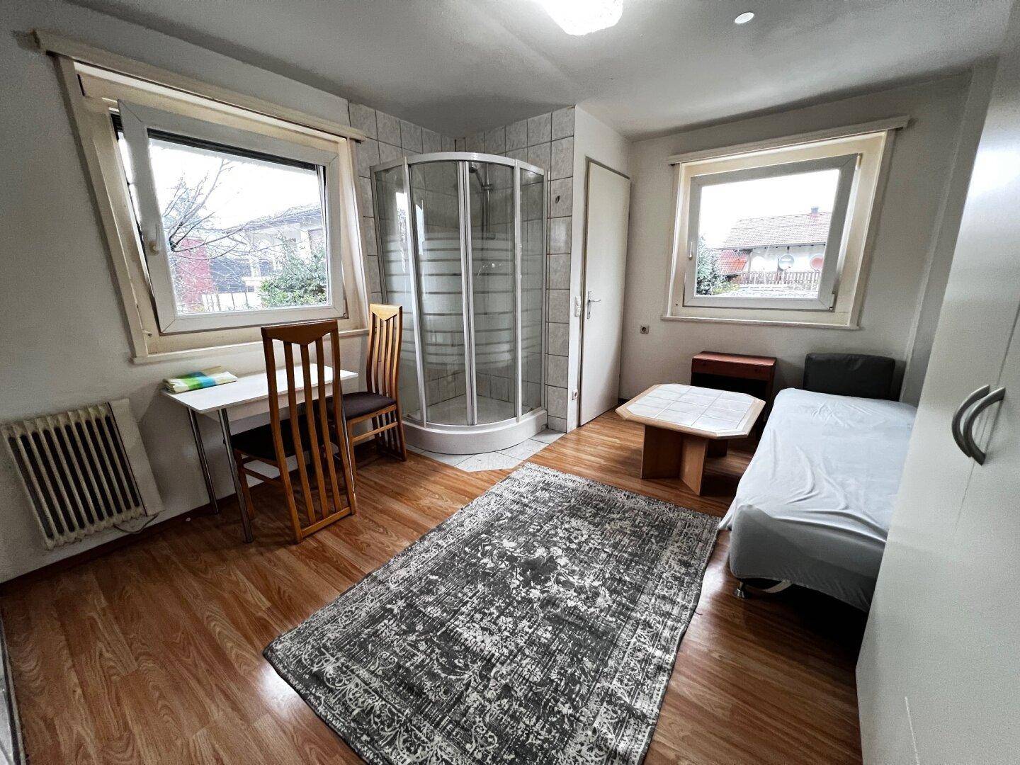 Helles Zimmer mit Laminatboden, Einzelbett und integrierter Duschkabine.