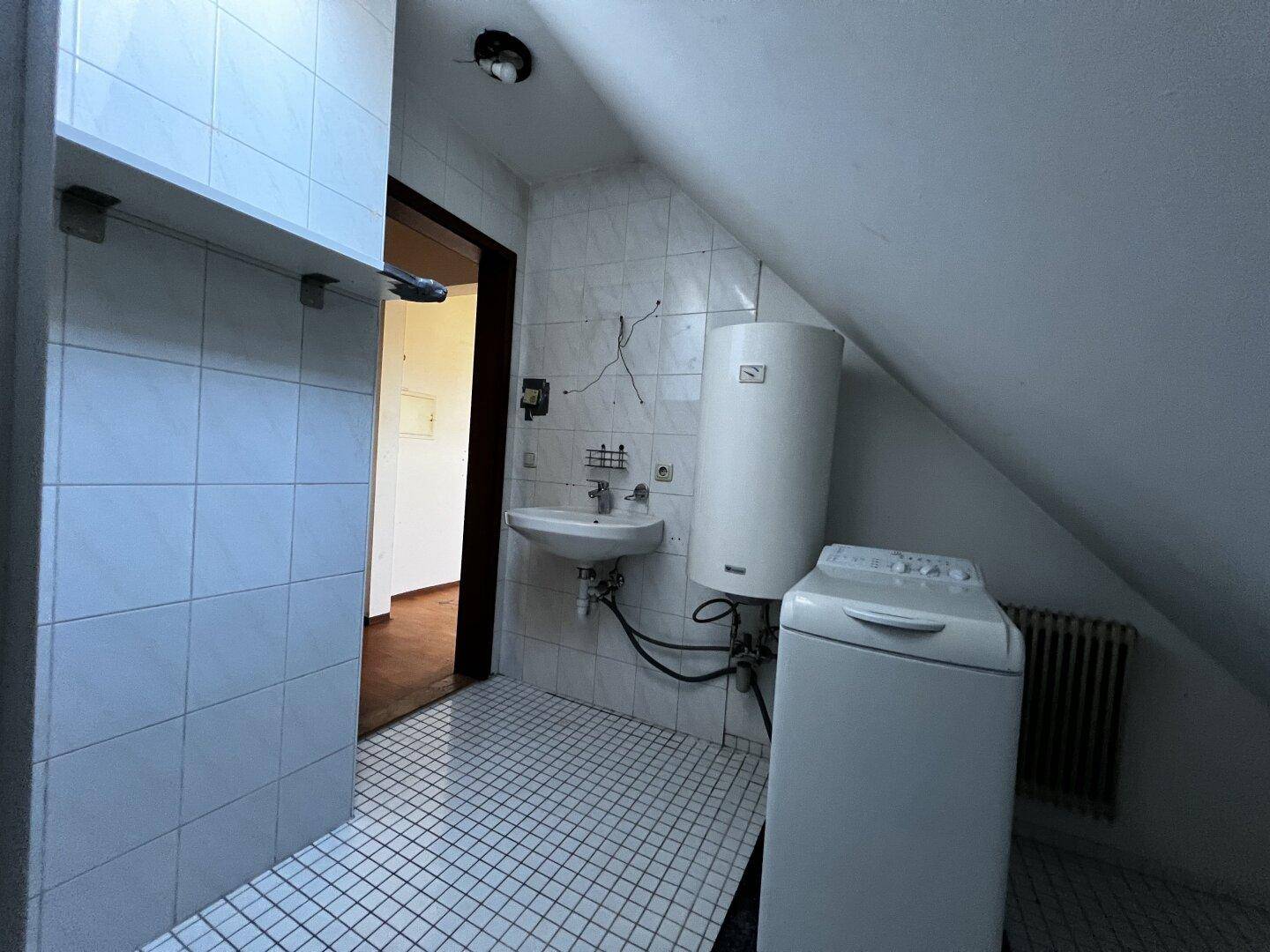 Dachgeschoss-Badezimmer mit Waschbecken, Waschmaschine und Heizkörper.