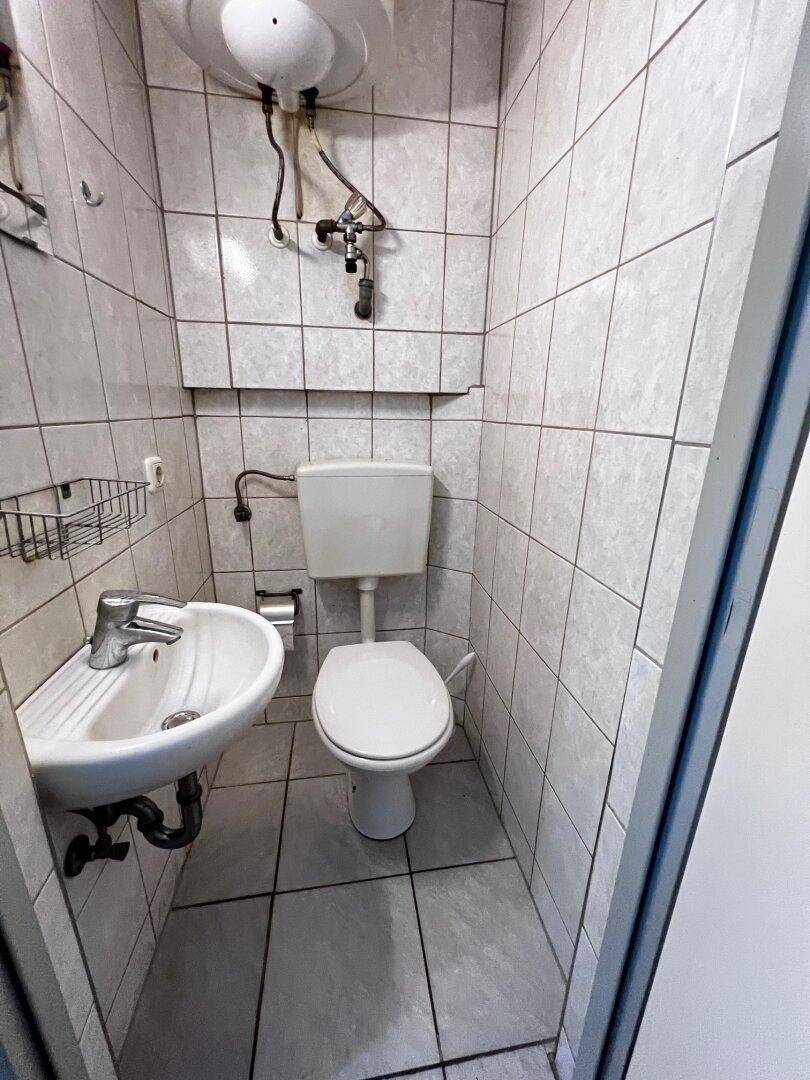 Kleines WC mit Waschbecken und Fliesen an Wänden und Boden.