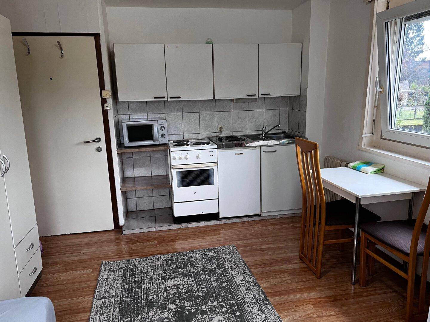 Studio-Apartment mit Küchenzeile, Esstisch und Laminatboden.