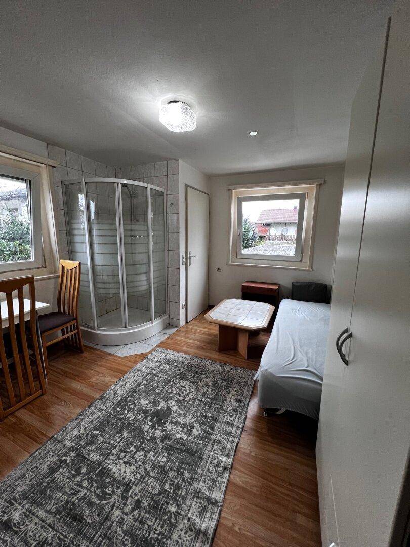 Studio-Apartment mit Bett, Duschkabine und Laminatboden.
