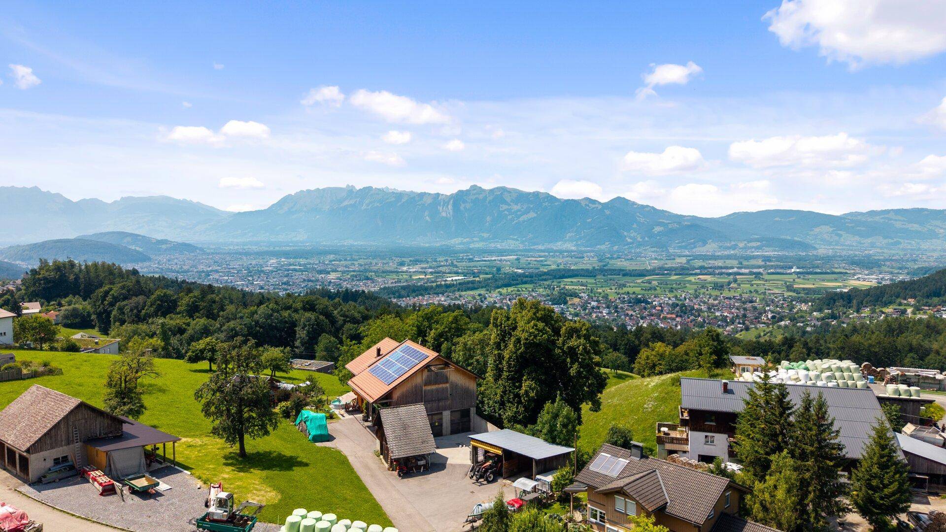 Luftaufnahme einer ländlichen Siedlung mit traditionellen Häusern und weitem Blick auf die Berglandschaft.