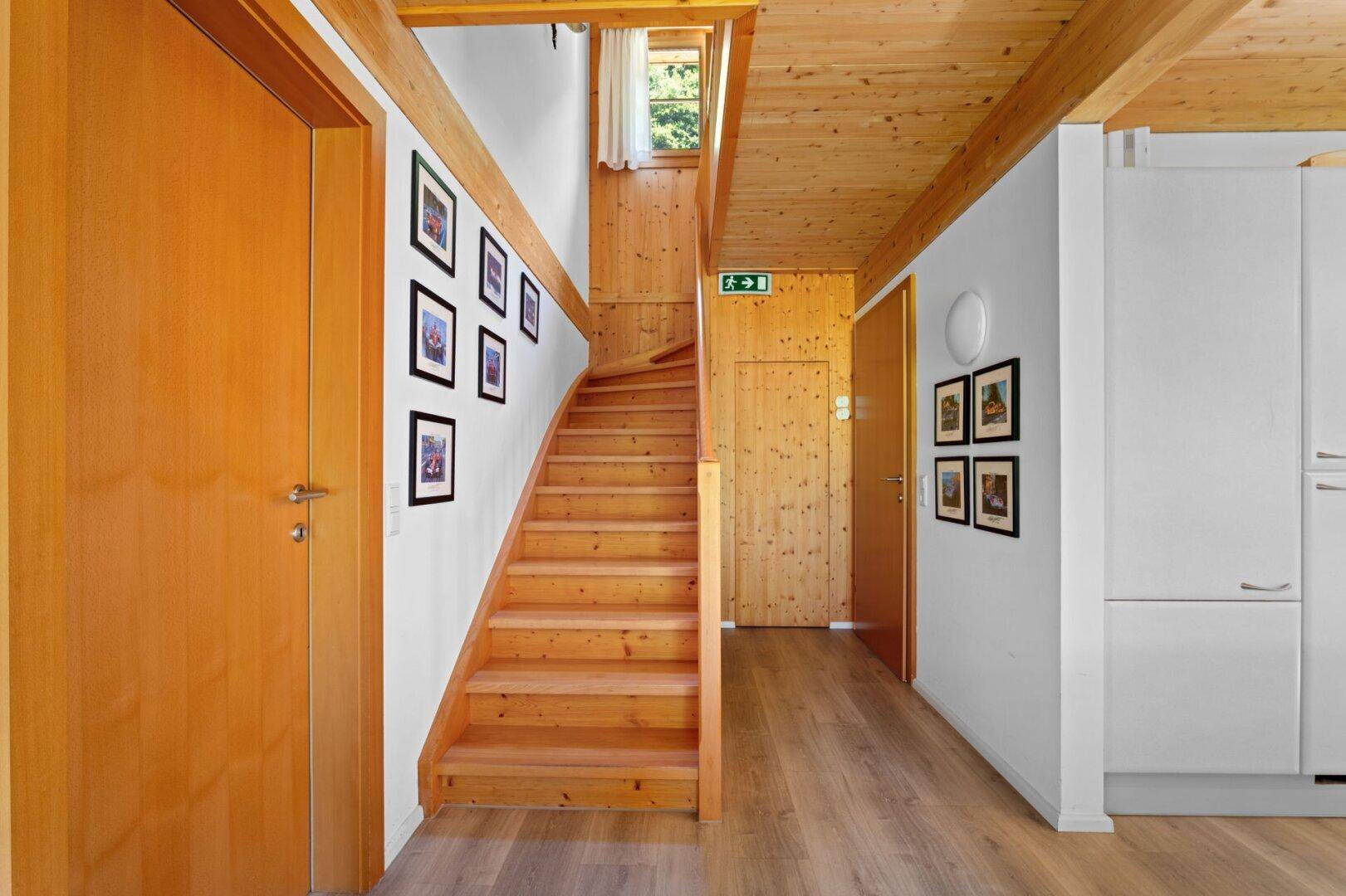 Heller Flur mit Holztreppe, Holzboden und gerahmten Bildern an der Wand.