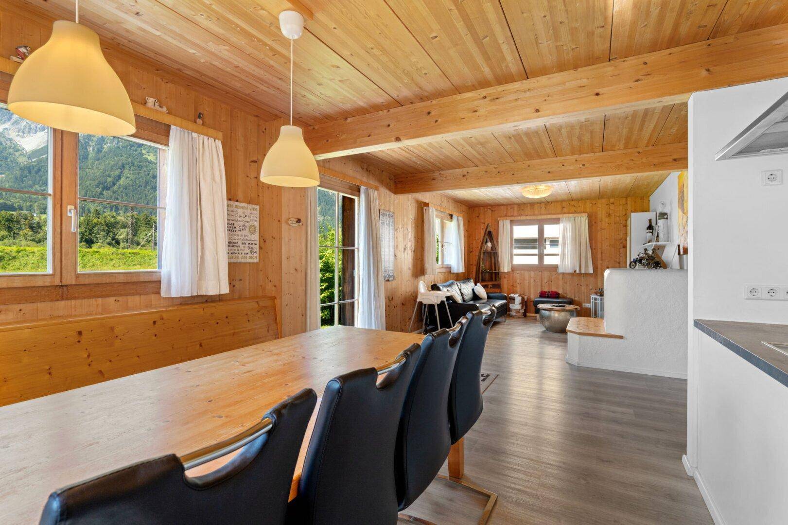 Heller Wohn- und Essbereich mit Holzbalkendecke, großem Esstisch und Bergblick.
