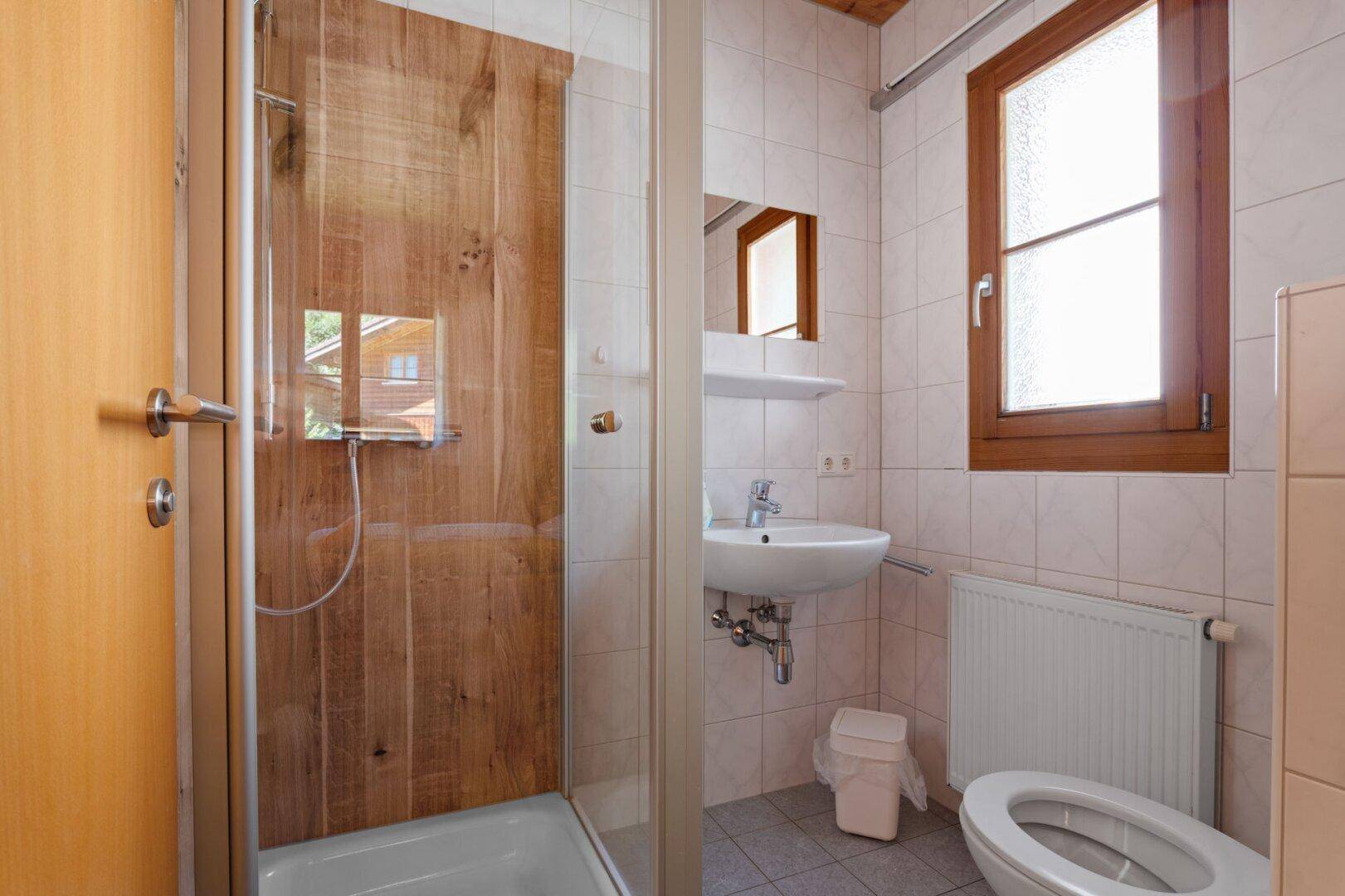 Kleines Badezimmer mit Dusche, WC, Waschbecken und Fenster in hellem Design.