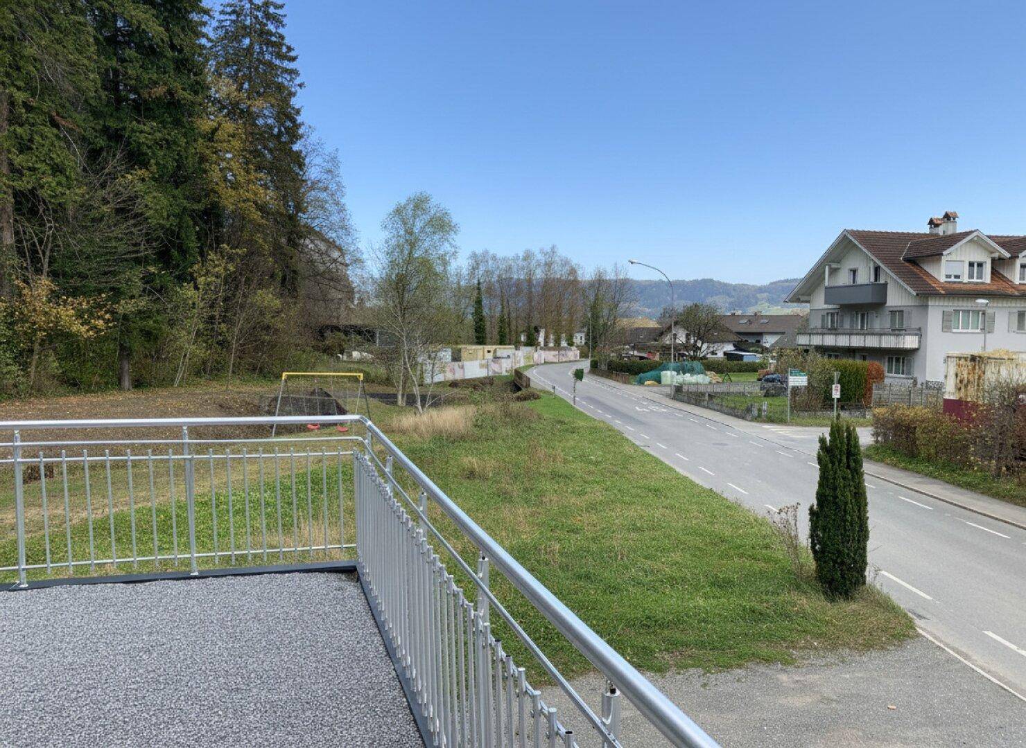 Terrasse mit Metallgeländer und weitem Blick auf die grüne Landschaft und eine Straße.