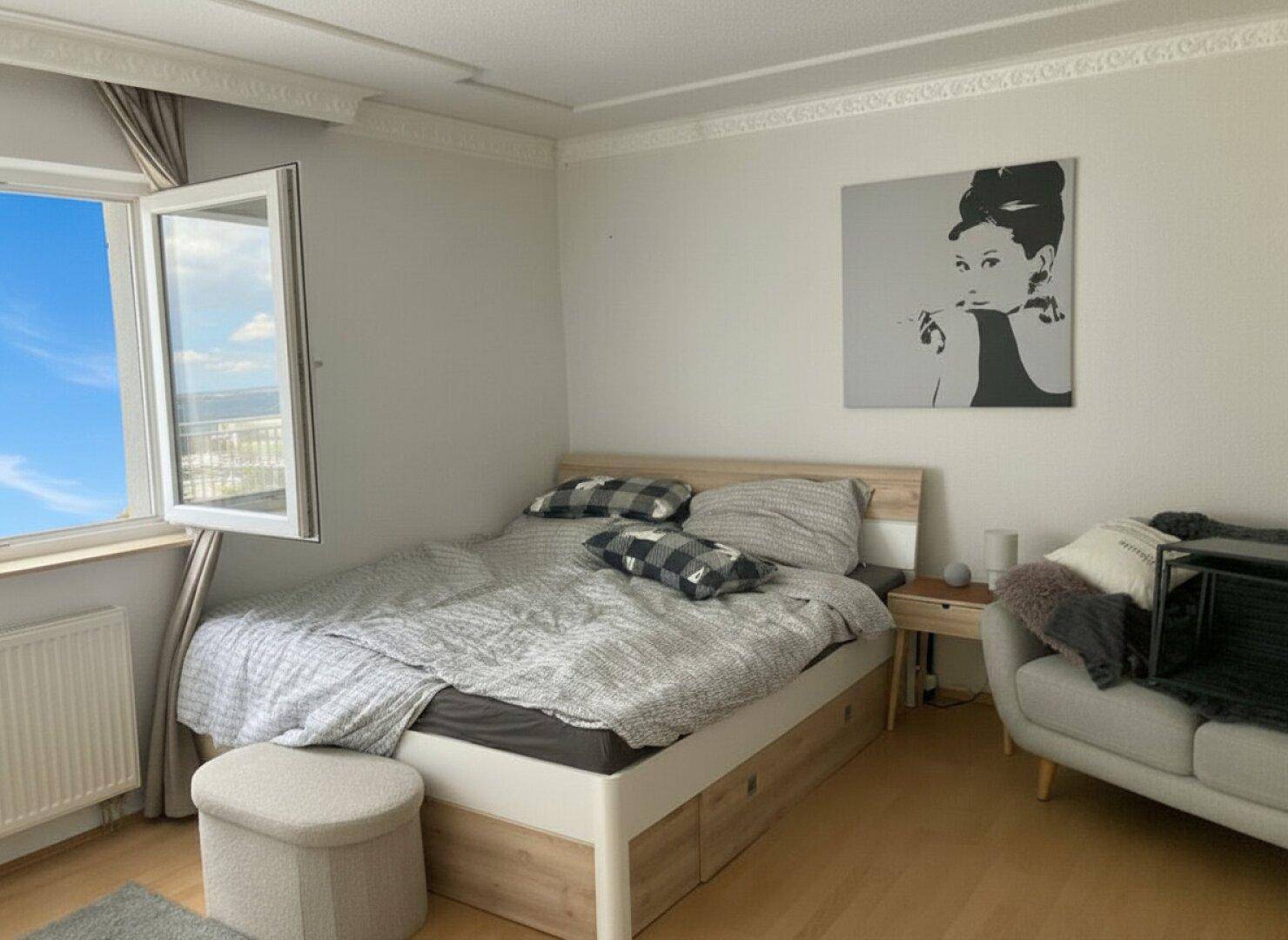 Schlafzimmer mit hellem Holzbett, Parkettboden und Fenster mit weitem Ausblick.